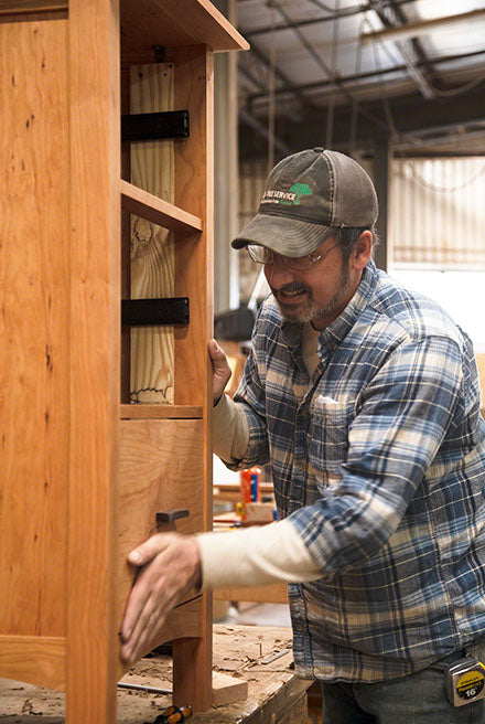 A man is working on a piece of furniture in a workshop.