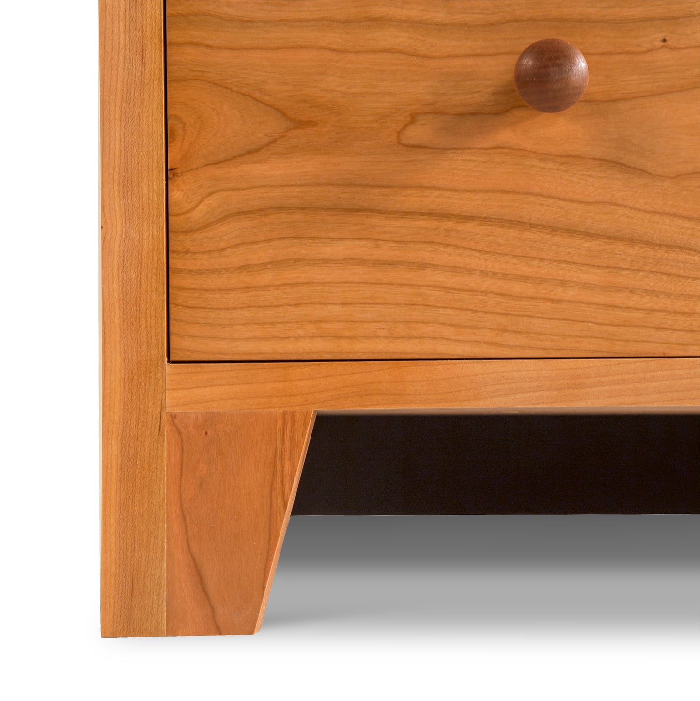 Close-up of a Lyndon Furniture American Country 6-Drawer Dresser - Floor Model featuring a smooth drawer with a round knob, and a sturdy leg, highlighting its simple yet elegant craftsmanship and natural wood grain.