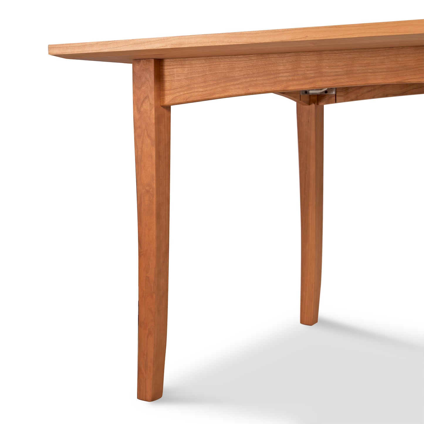 A close-up view of a Maple Corner Woodworks American Shaker Rectangular Solid Top Table, focusing on the corner section where the smooth tabletop meets the simple, straight leg. The background is plain white, emphasizing.