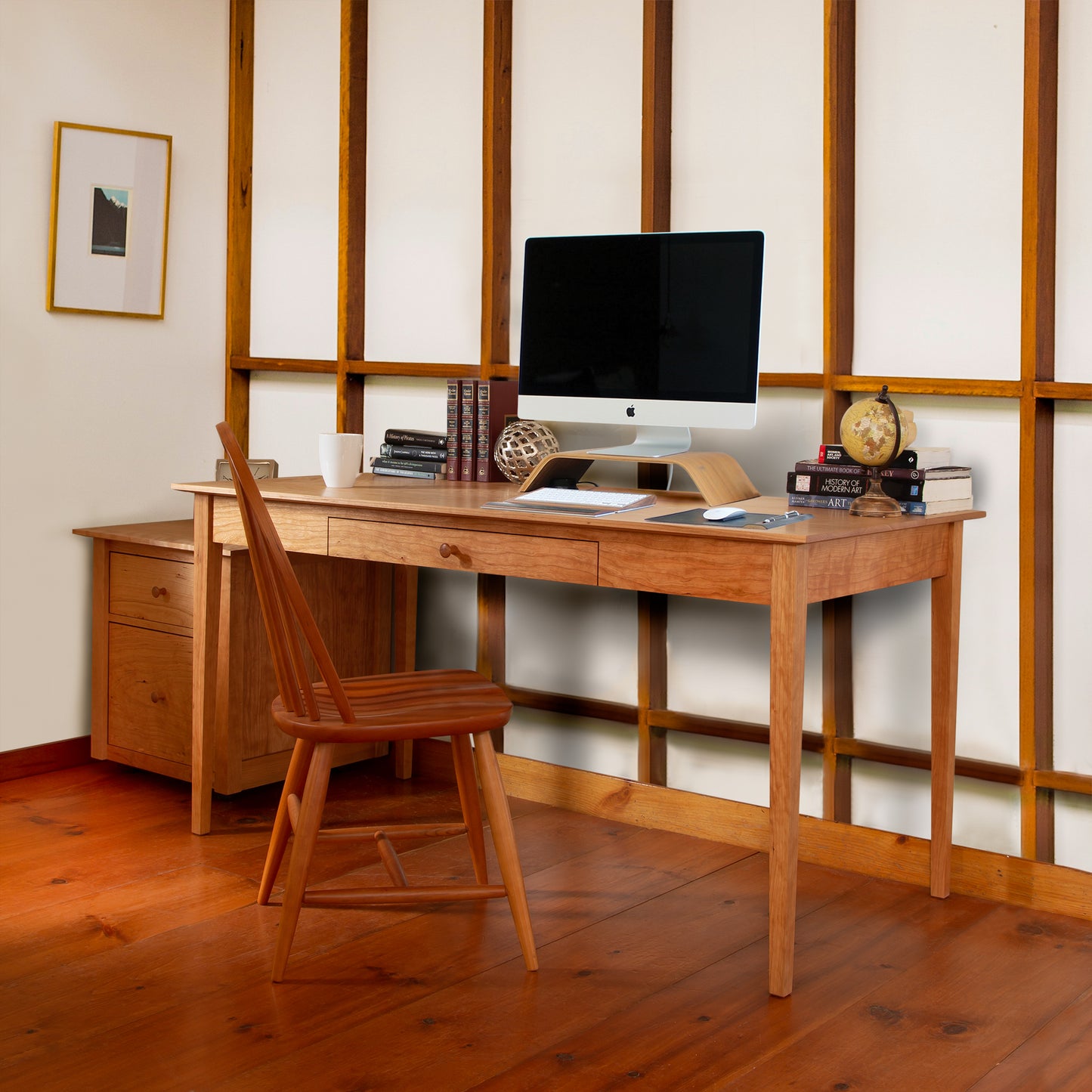 A tidy home office setup features a Maple Corner Woodworks American Shaker Writing Desk, imac computer, and a wooden chair on sustainably harvested hardwood floor, accented by minimalistic decor and framed art on the wall.