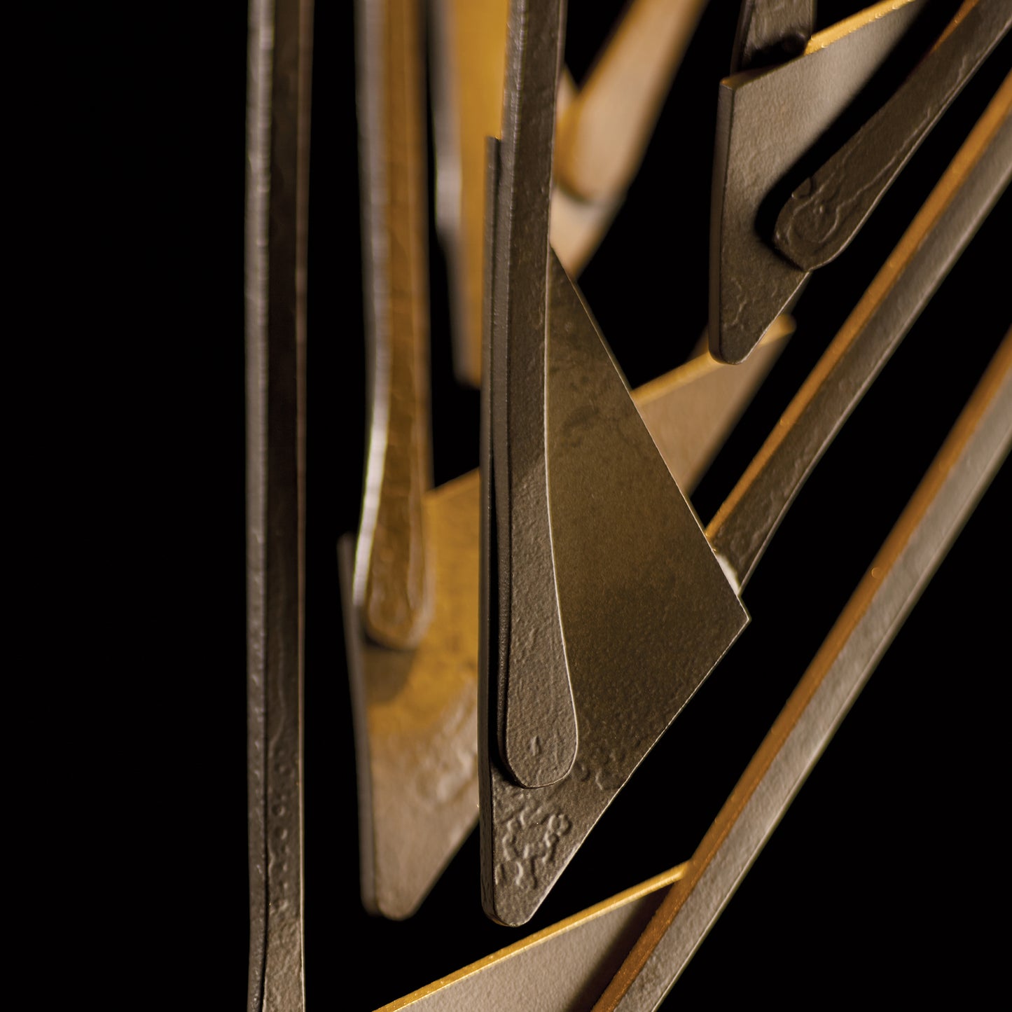 A close up of a Hubbardton Forge Amulet Mini Pendant metal sculpture with a black background.