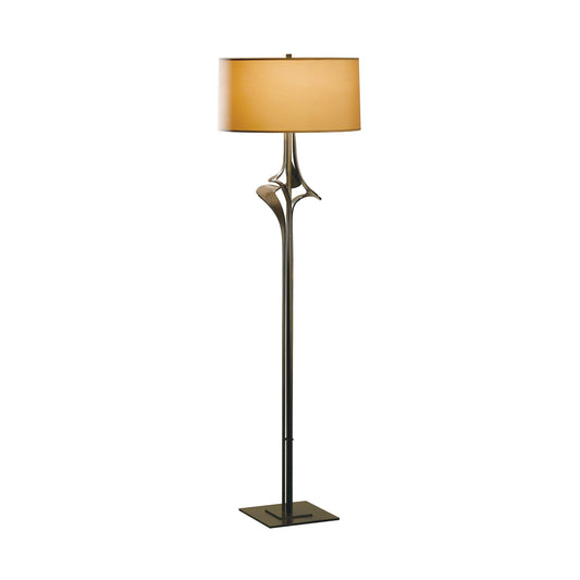 An Antasia Floor Lamp by Hubbardton Forge with a metal base and a beige shade.