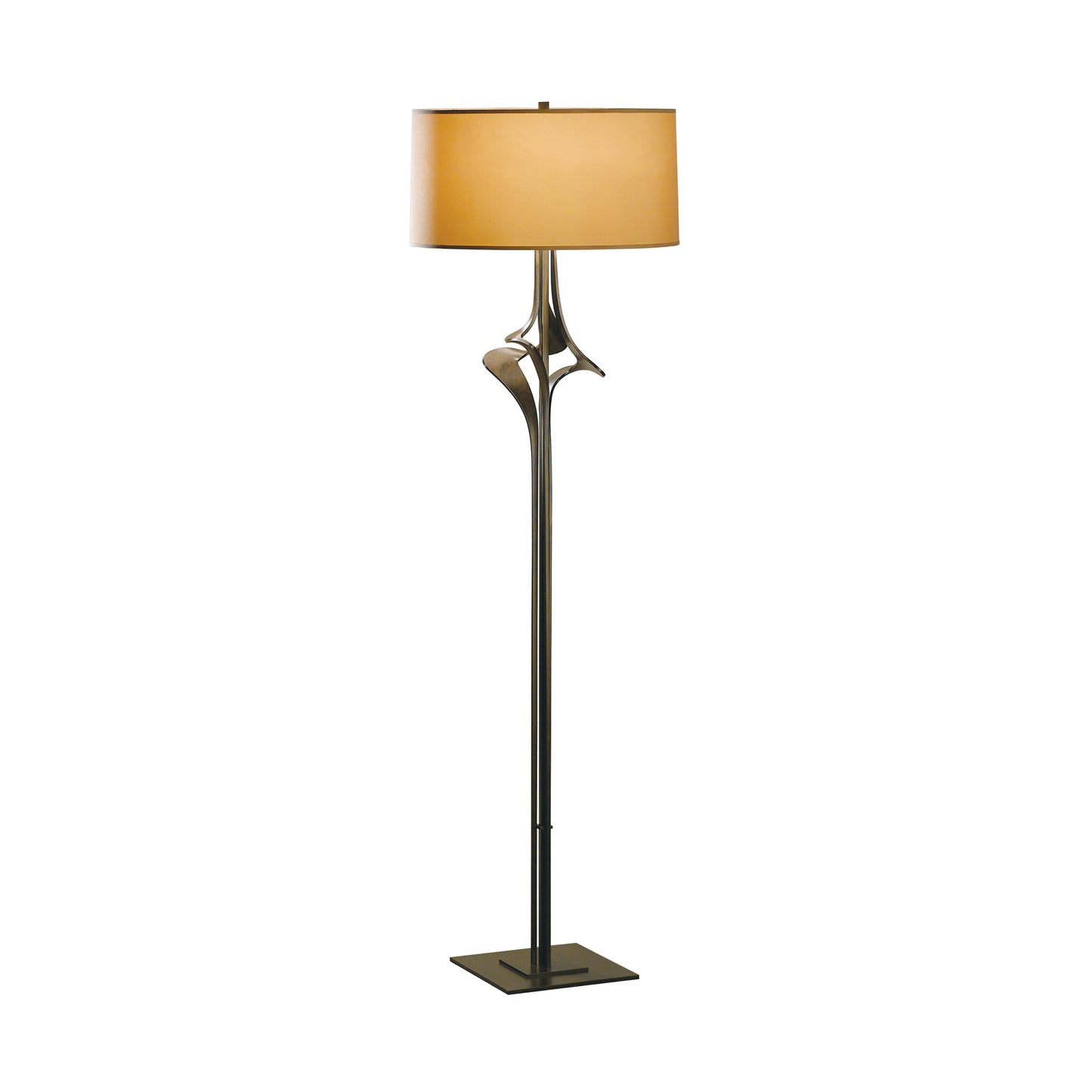 A modern Hubbardton Forge Antasia Floor Lamp with a slender black base and curving metallic accents, topped by a wide, cylindrical beige shade. The design suggests elegance and simplicity.