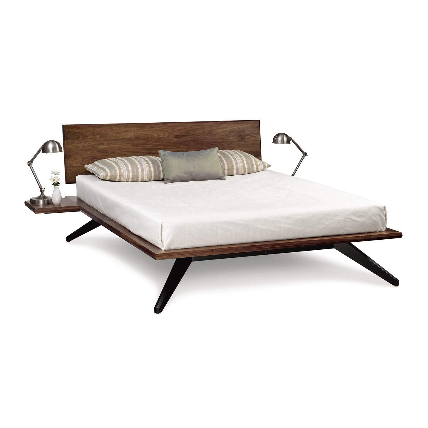 Modern solid walnut wood Astrid platform bed with a white mattress, two striped pillows, and a gray accent pillow, flanked by two identical nightstands with lamps from the Copeland Furniture Astrid Bedroom Furniture Collection, isolated.