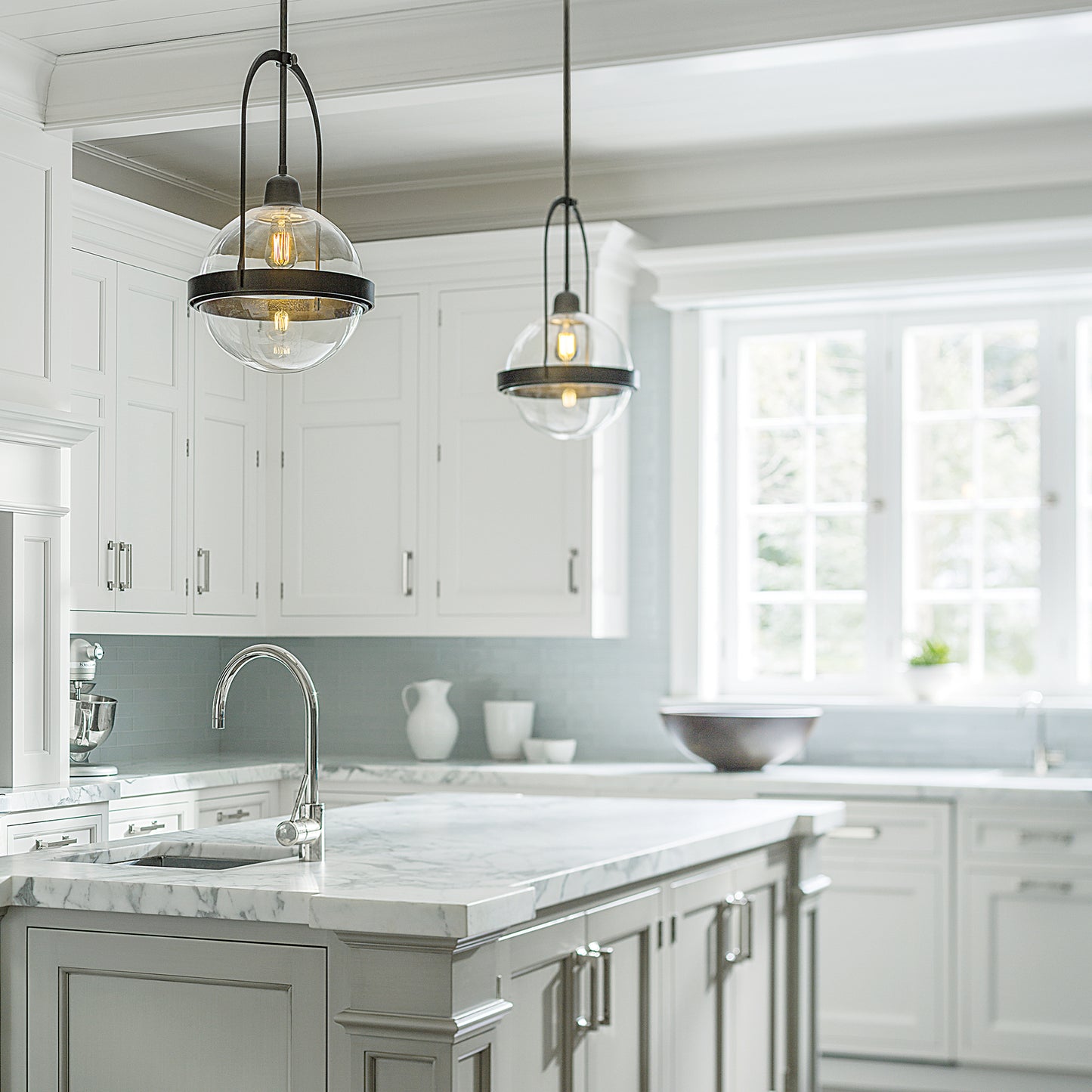 Hubbardton Forge Atlas Mini Pendants hanging over a marble kitchen island with modern design and white cabinetry.