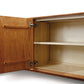 An open wooden cabinet with empty shelves and visible hinges, handcrafted as part of the Audrey 4-Door Buffet collection by Copeland Furniture.