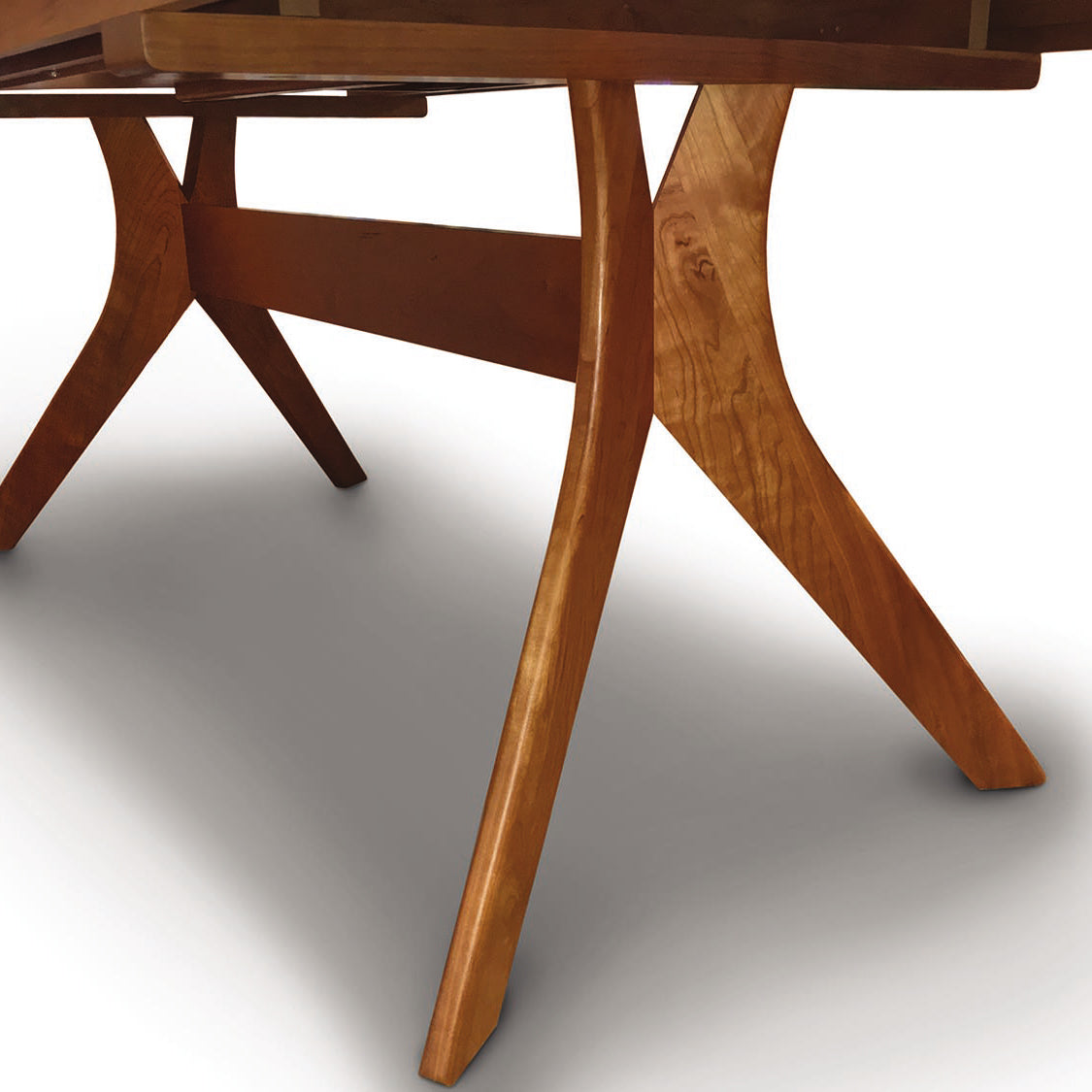 Close-up of a solid cherry wood Audrey Extension Dining Table by Copeland Furniture showing detail of the grain and structure of the legs and underside.