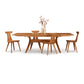 A solid cherry wood Audrey Extension Dining Table set with six Copeland Furniture chairs and a vase of flowers on top, isolated on a white background.