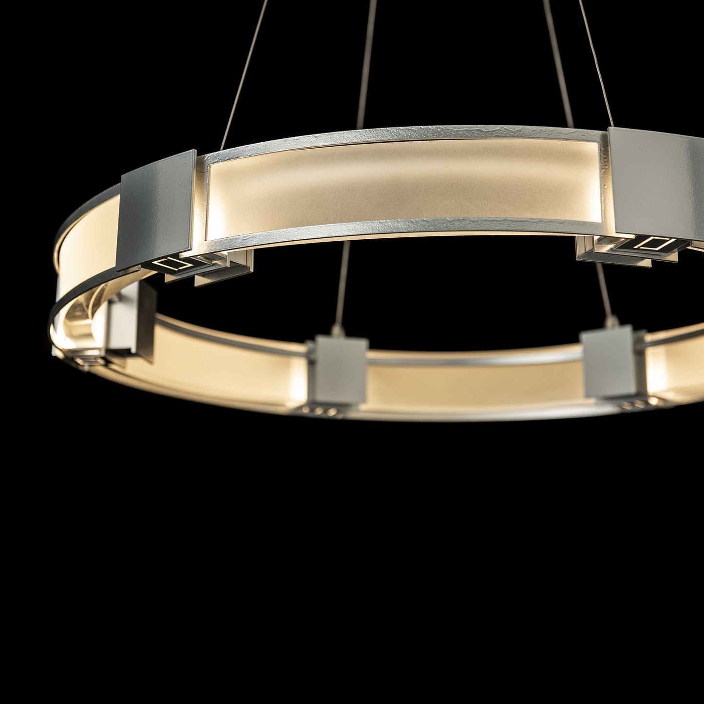 Aura Glass Pendant by Hubbardton Forge features a circular metallic frame with warm, diffused lighting.