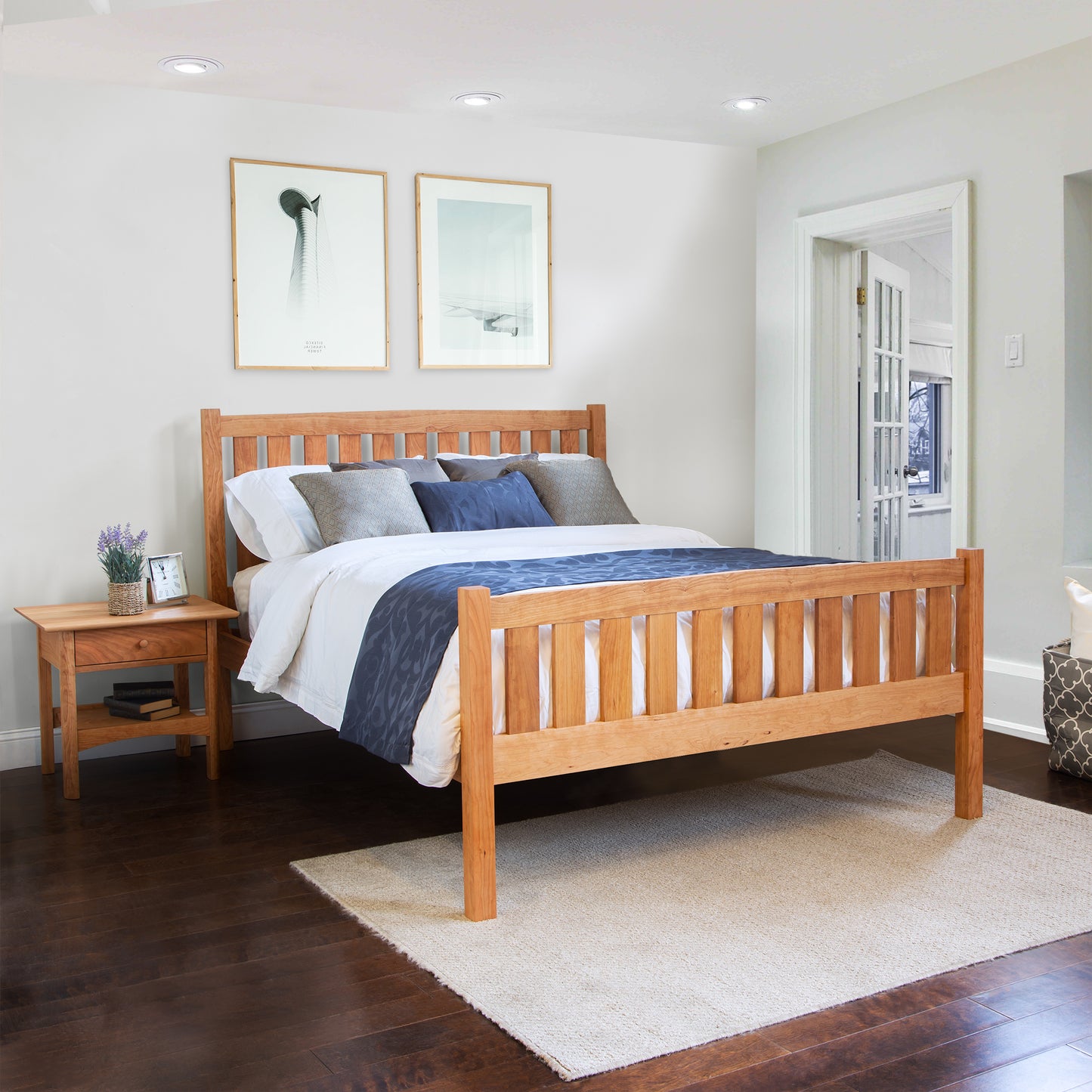 Bennington Bed with High Footboard by Vermont Furniture Designs, featuring white and gray bedding, showcases its elegant wood craftsmanship. Nightstand partially visible.