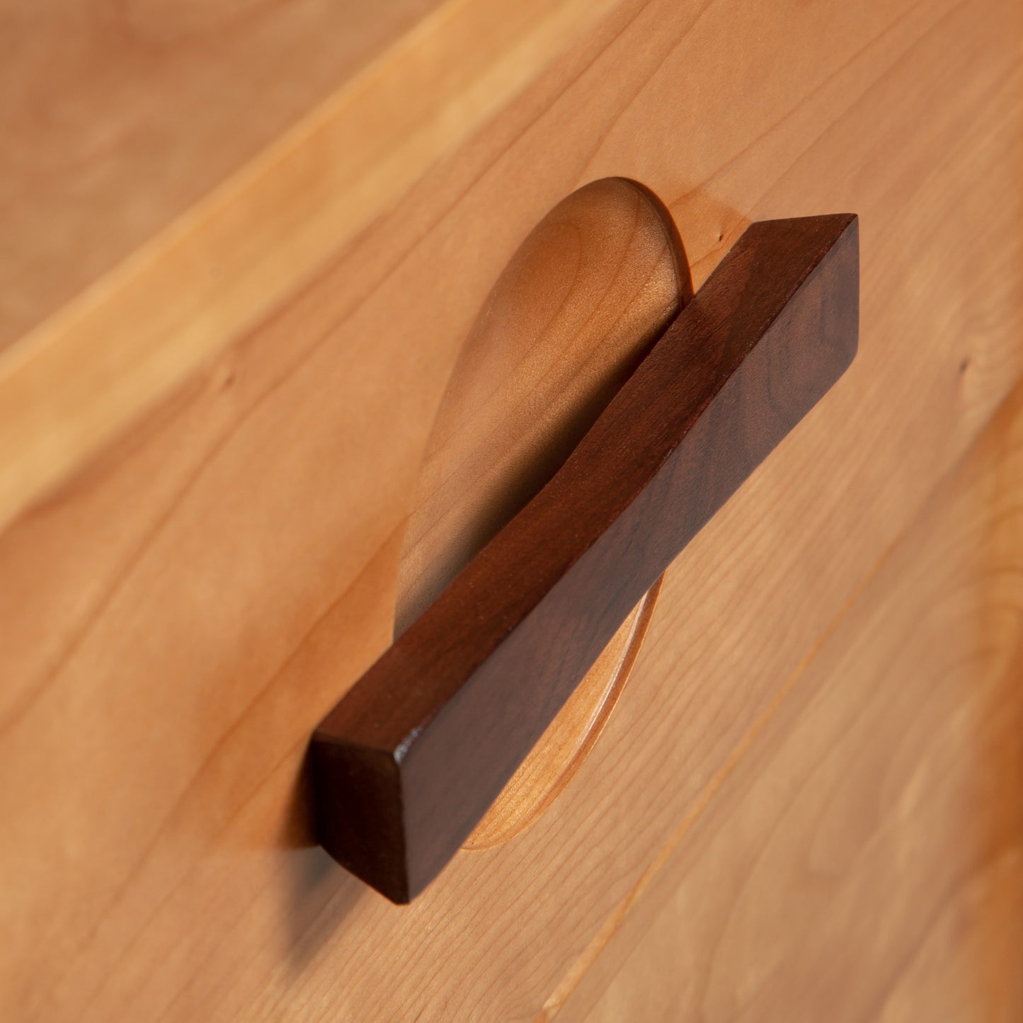A Copeland Furniture Berkeley nightstand drawer knob mounted on a wooden cabinet drawer with a visible grain, angled to show the profile of the handle, reflecting the American Arts & Crafts style.