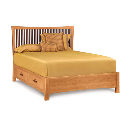 A Berkeley Cherry Storage Bed by Copeland Furniture in the American Craftsman style, with a slatted headboard, fitted with a yellow bedsheet and pillows, and featuring under-bed storage at the footend.