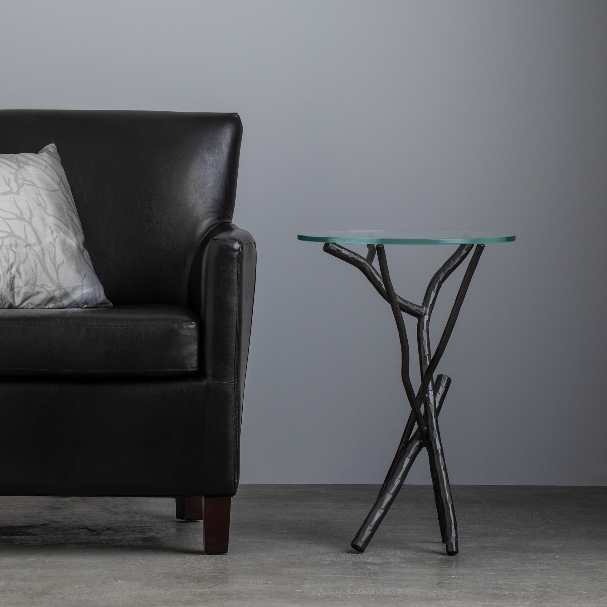 Black leather couch with a silver pillow beside the Hubbardton Forge Brindille Accent Table.