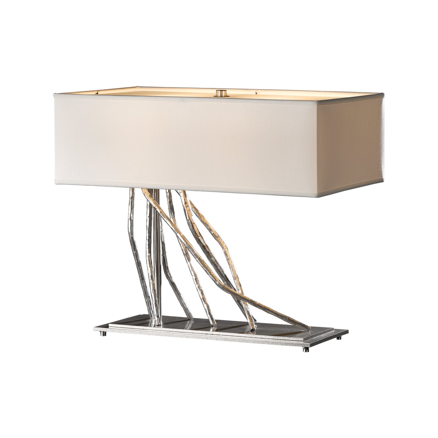 A modern hand-forged Brindille Table Lamp with a rectangular beige shade and a unique metallic base featuring intertwined iron rods on a reflective platform by Hubbardton Forge.