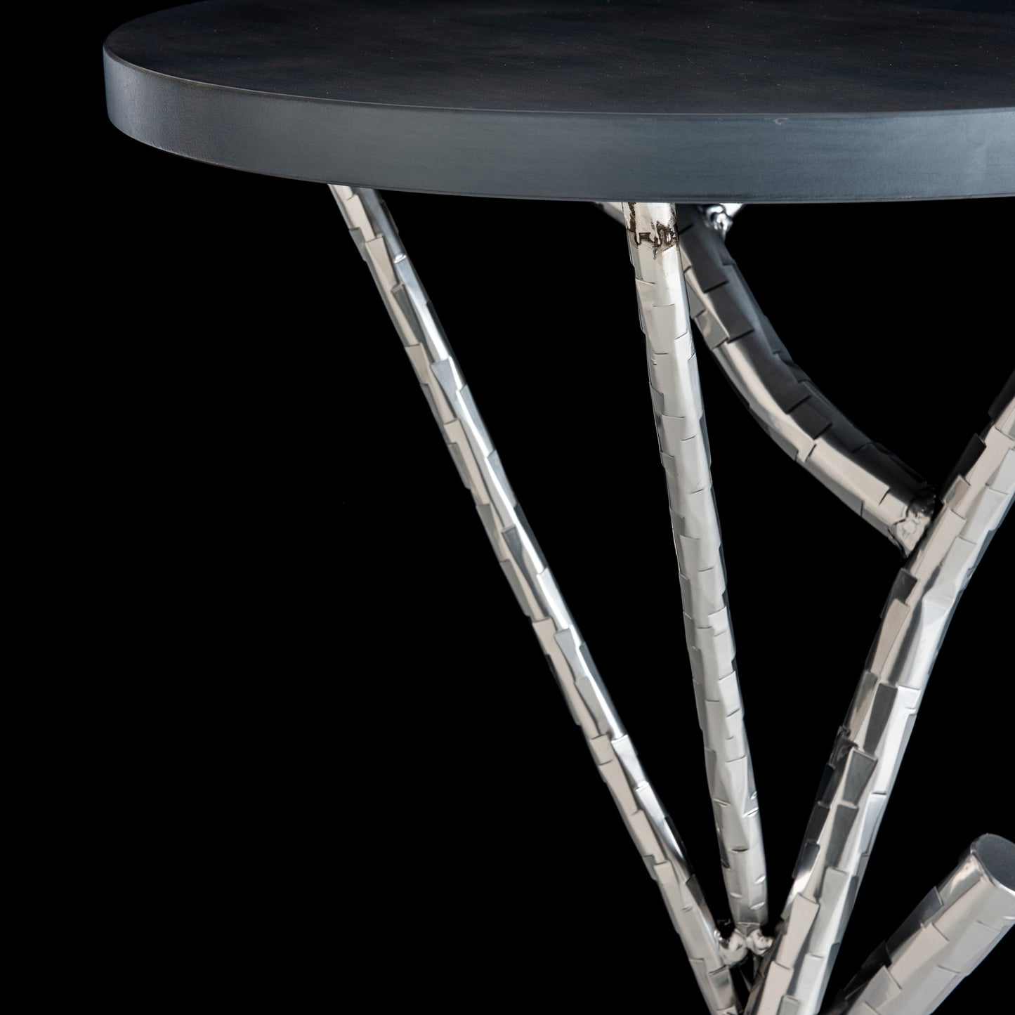 Brindille Wood Top Accent Table by Hubbardton Forge with a textured black tabletop, metal legs, and hand-hammered steel base.