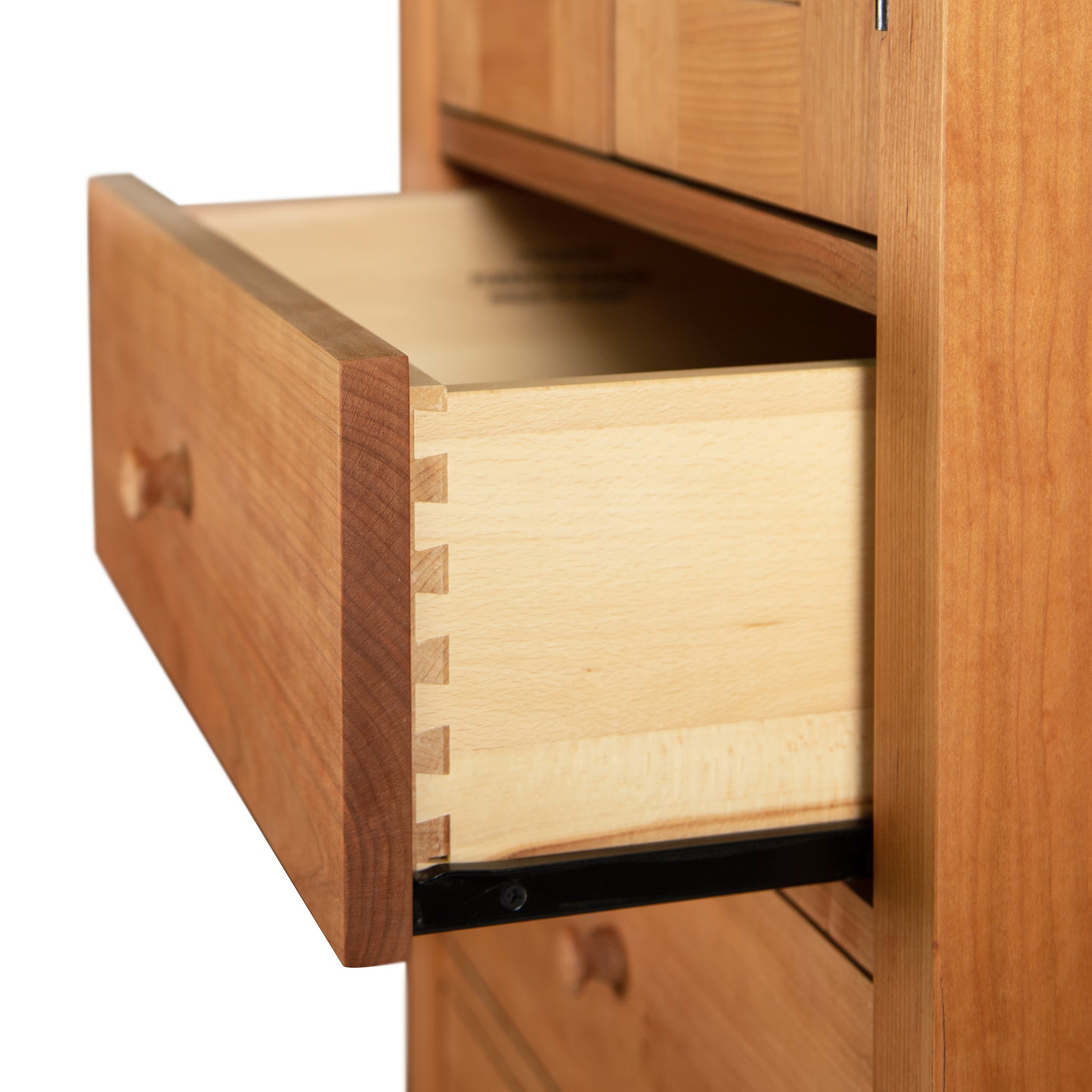 An open Burlington Shaker Tall Storage Chest drawer showcasing dovetail joints, with other drawers in the background. (Brand Name: Vermont Furniture Designs)