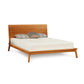 A modern Copeland Furniture Catalina Cherry Platform Bed frame of solid natural cherry hardwood with a simple headboard, supporting a white mattress and adorned with three pillows, isolated against a white background.
