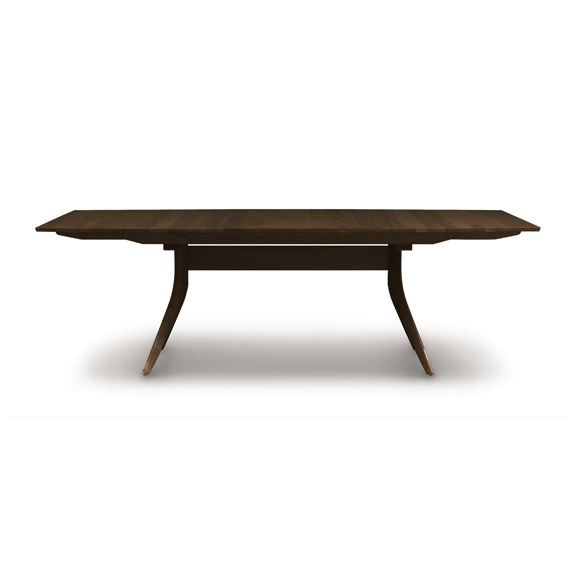 A solid American hardwood dining table with a dark finish and an extended leaf, featuring tapered legs and a smooth tabletop, isolated on a white background - the Catalina Trestle Extension Table by Copeland Furniture.
