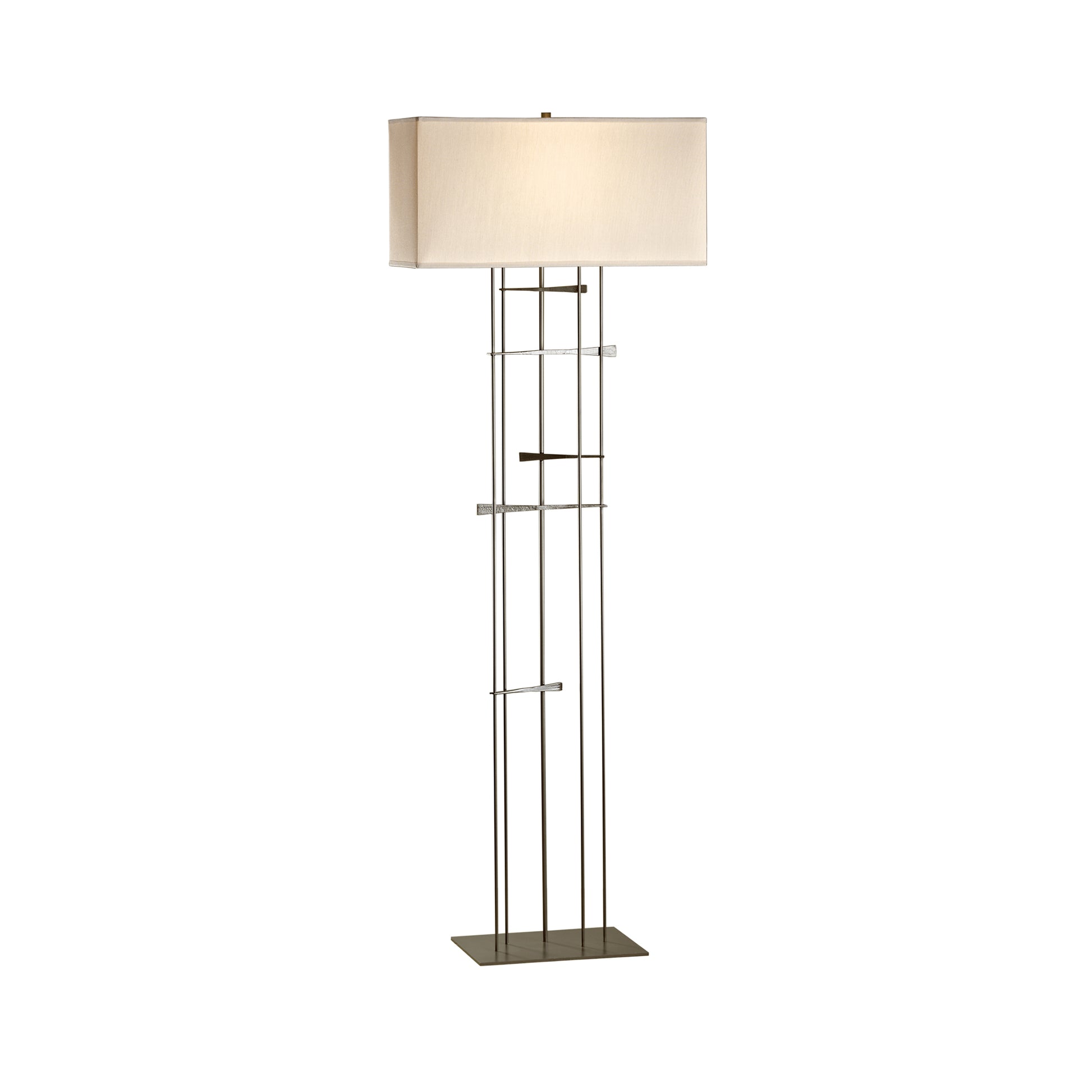 A Hubbardton Forge Cavaletti Floor Lamp with a rectangular beige shade and a metal finish base featuring a unique, geometric design of overlapping squares and rectangles.