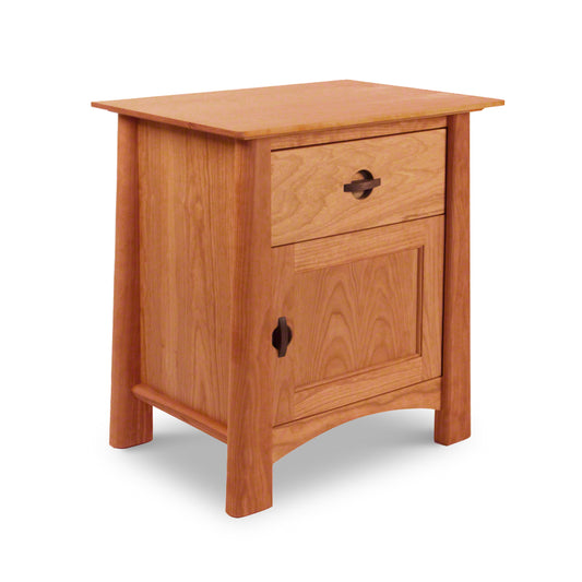 A Maple Corner Woodworks Cherry Moon 1-Drawer Nightstand With Door, crafted from solid wood by a Vermont craftsman, features a smooth top, a single drawer with a knob, and a cabinet below with a wooden handle, set against a