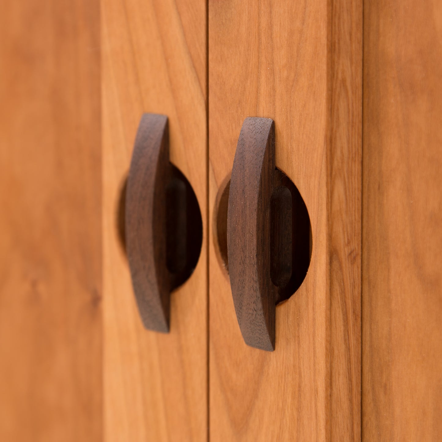 Close-up view of two round, dark solid hardwood door knobs on a Maple Corner Woodworks Cherry Moon Small 38" Sideboard. The focus is on the texture and natural grain of the wood.