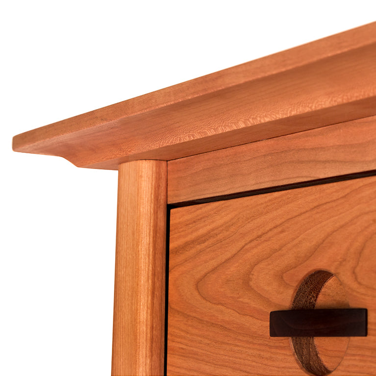 Close-up view of a Maple Corner Woodworks Cherry Moon 5-Drawer Chest showing the corner with detailed grain patterns and a round handle, isolated on a white background.