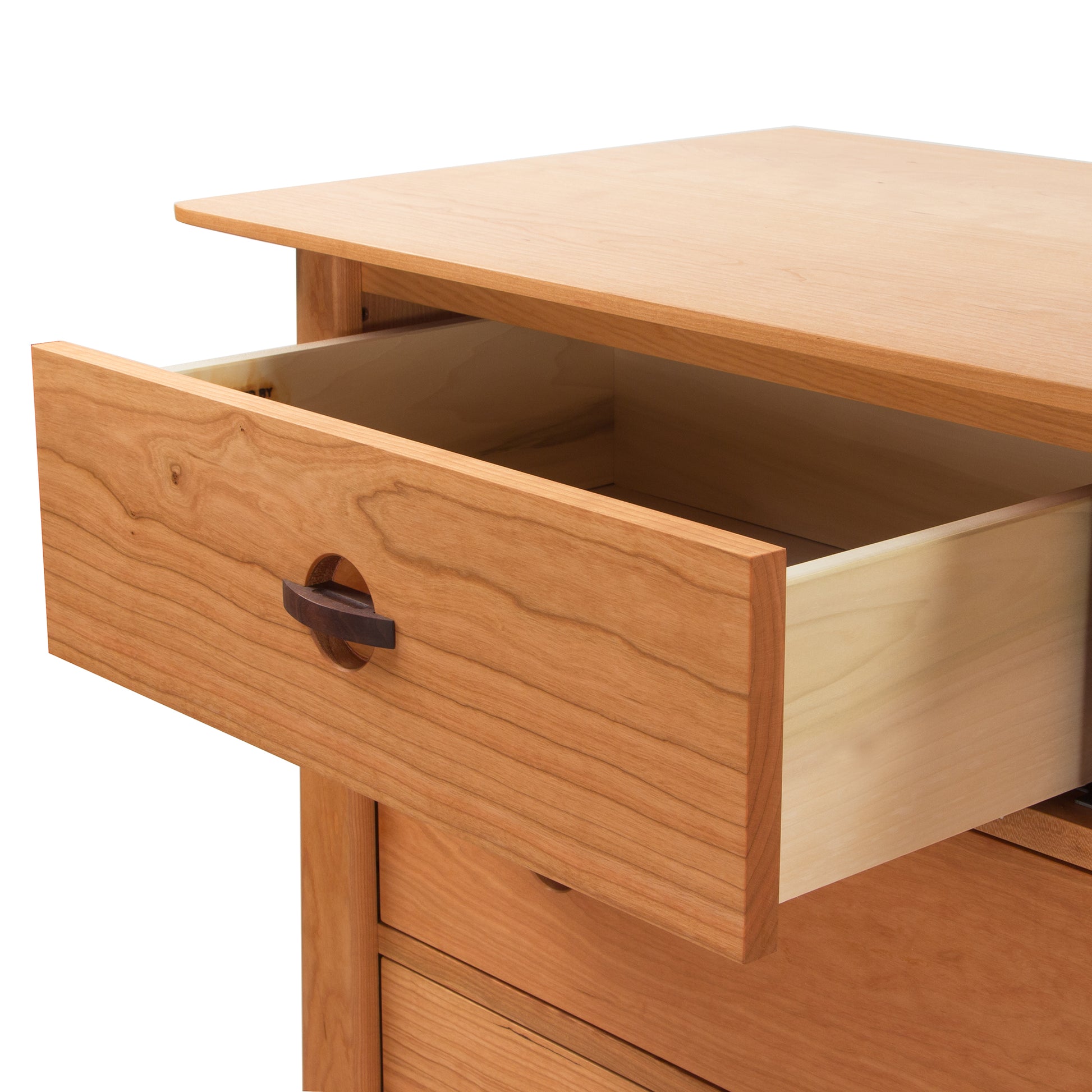 A close-up of an open drawer in a Cherry Moon 7-Drawer Dresser by Maple Corner Woodworks, showing fine wood grain and a simple wooden handle. The background is plain white, emphasizing the natural color and texture of the sustainably harvested wood.