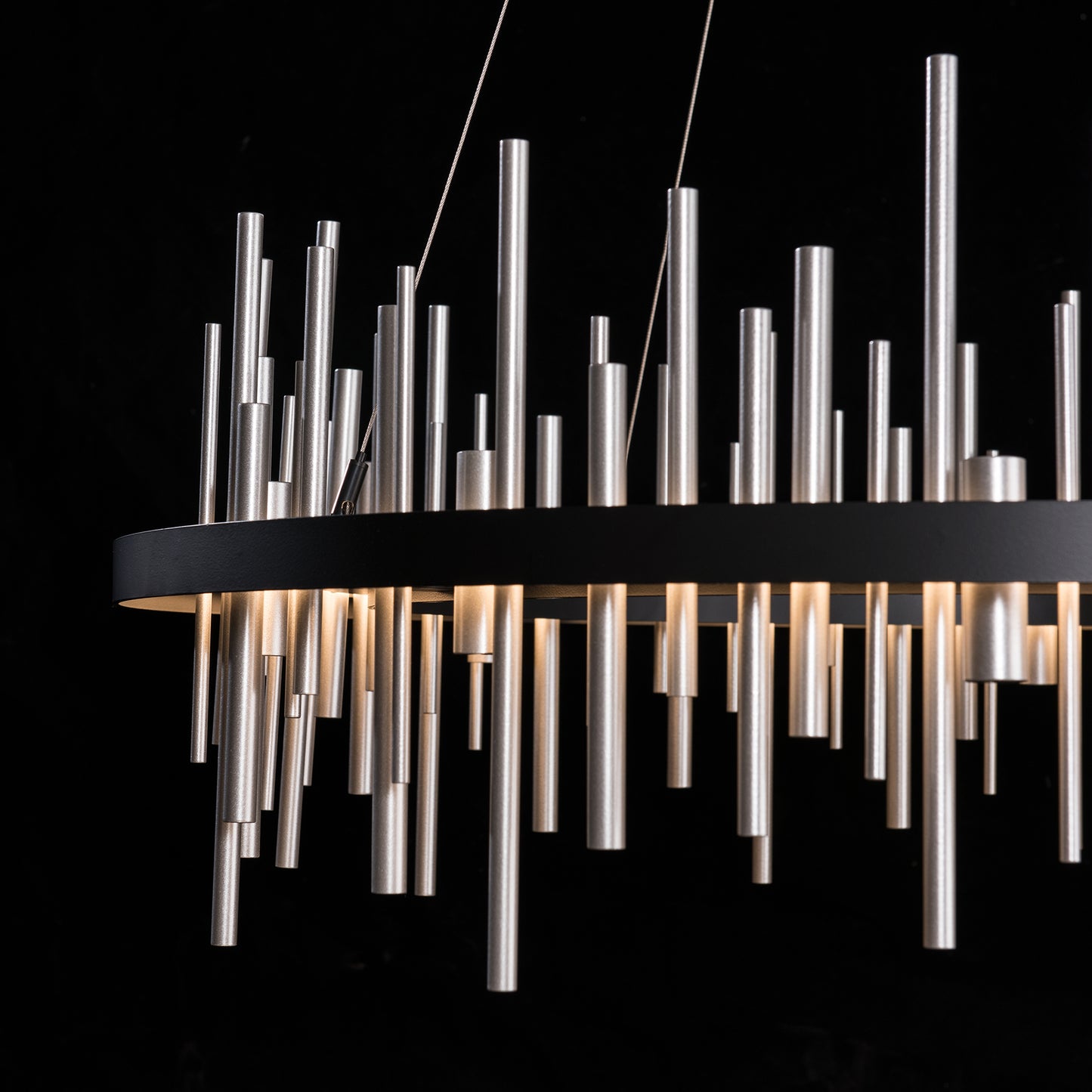 Circular Cityscape Pendant by Hubbardton Forge: Modern chandelier featuring cylindrical metal rods on a circular frame, emitting warm light.
