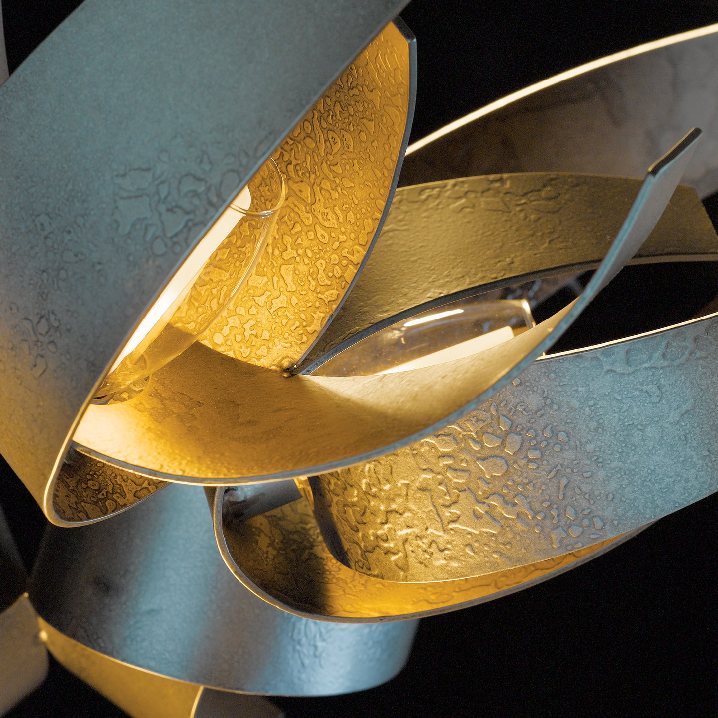 Hubbardton Forge Corona Pendant with intertwined metallic gold and silver ribbons, textured surface, and warm glow.