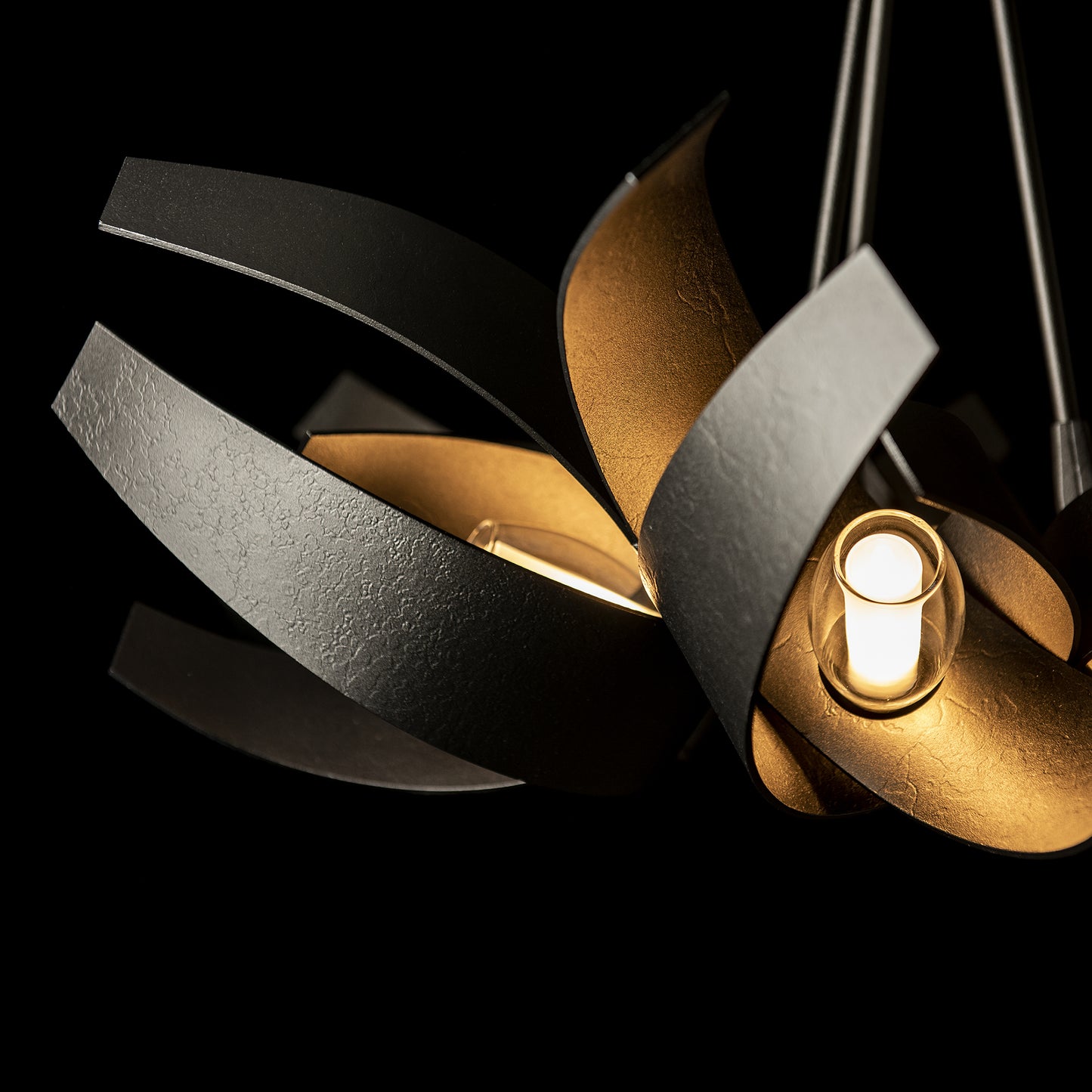 Hubbardton Forge Corona Pendant with elegant black and gold petals and glowing lights.