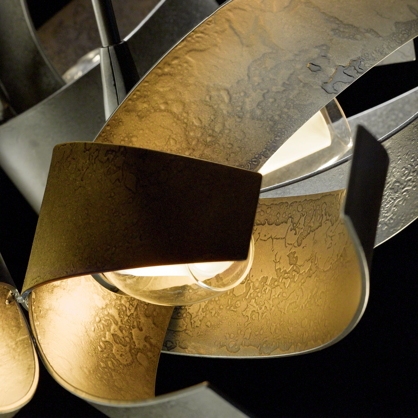 Hubbardton Forge Corona Pendant with artistic curling metal strips encircling a glowing bulb.