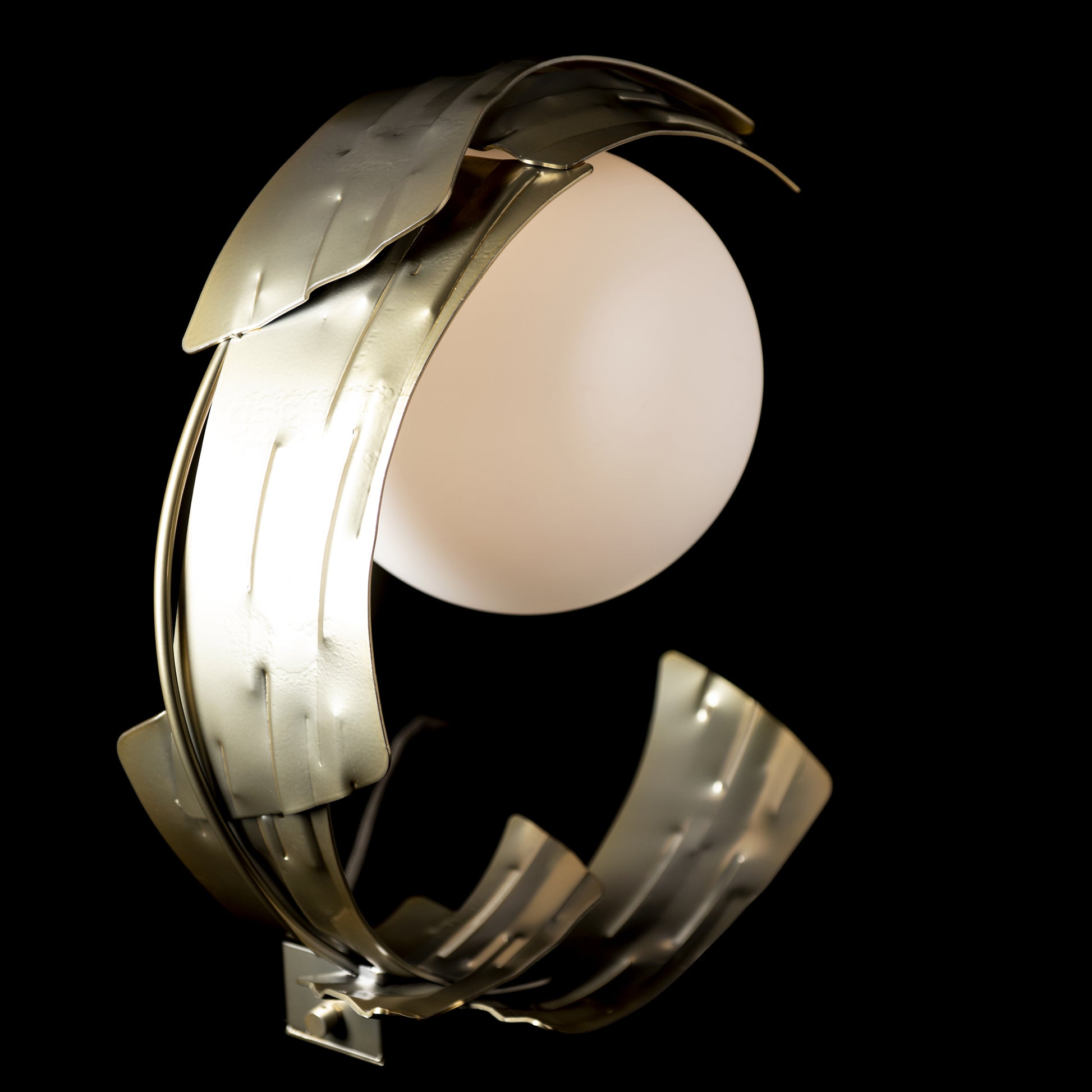 Hubbardton Forge Crest Table Lamp featuring a glowing sphere with intricate cutouts and a shiny metallic ring design.
