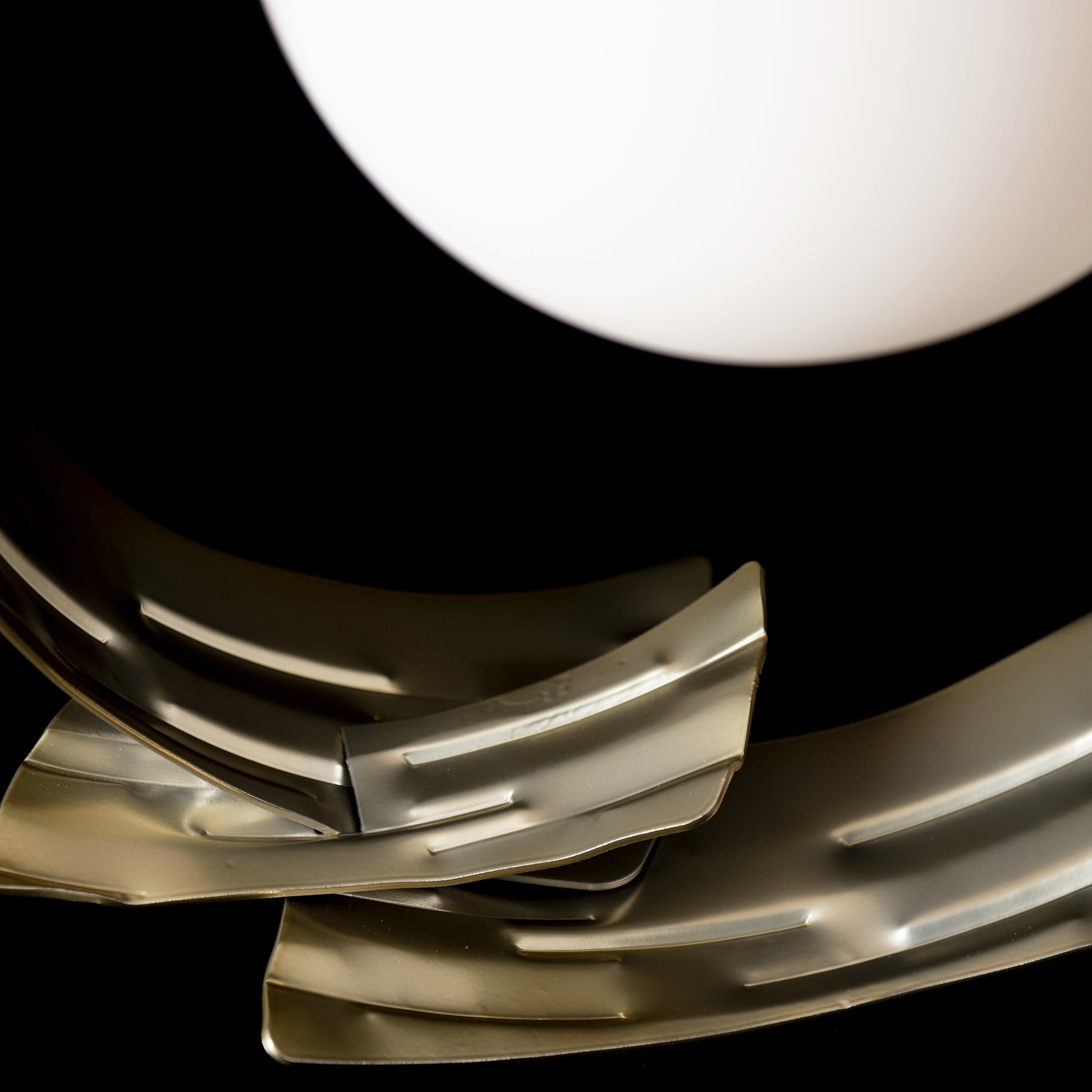 Curved steel sculpture with hand-forged design, elegantly illuminated by a Hubbardton Forge Crest Table Lamp, showcasing intricate craftsmanship.