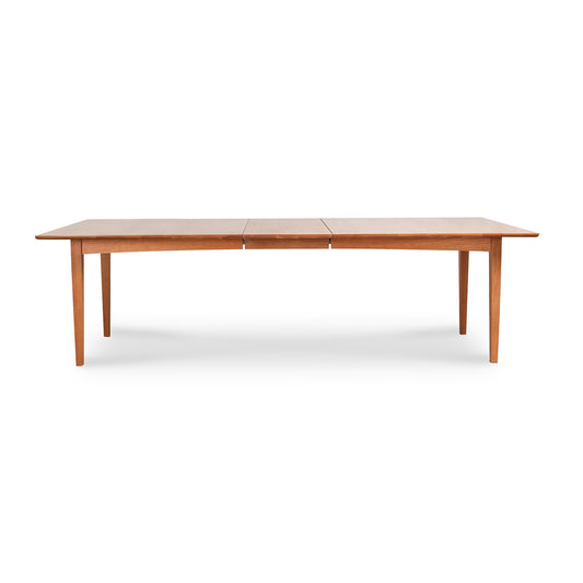 An elegant wooden dining table, the Custom Heartwood Shaker Extension Dining Table - 42"x84" - Clearance by Vermont Furniture Designs, is crafted from solid maple wood. It features an extended leaf in the center and has a rectangular shape. The table stands on four tapered legs and boasts a smooth, eco-friendly oil finish that highlights the natural beauty of maple wood.