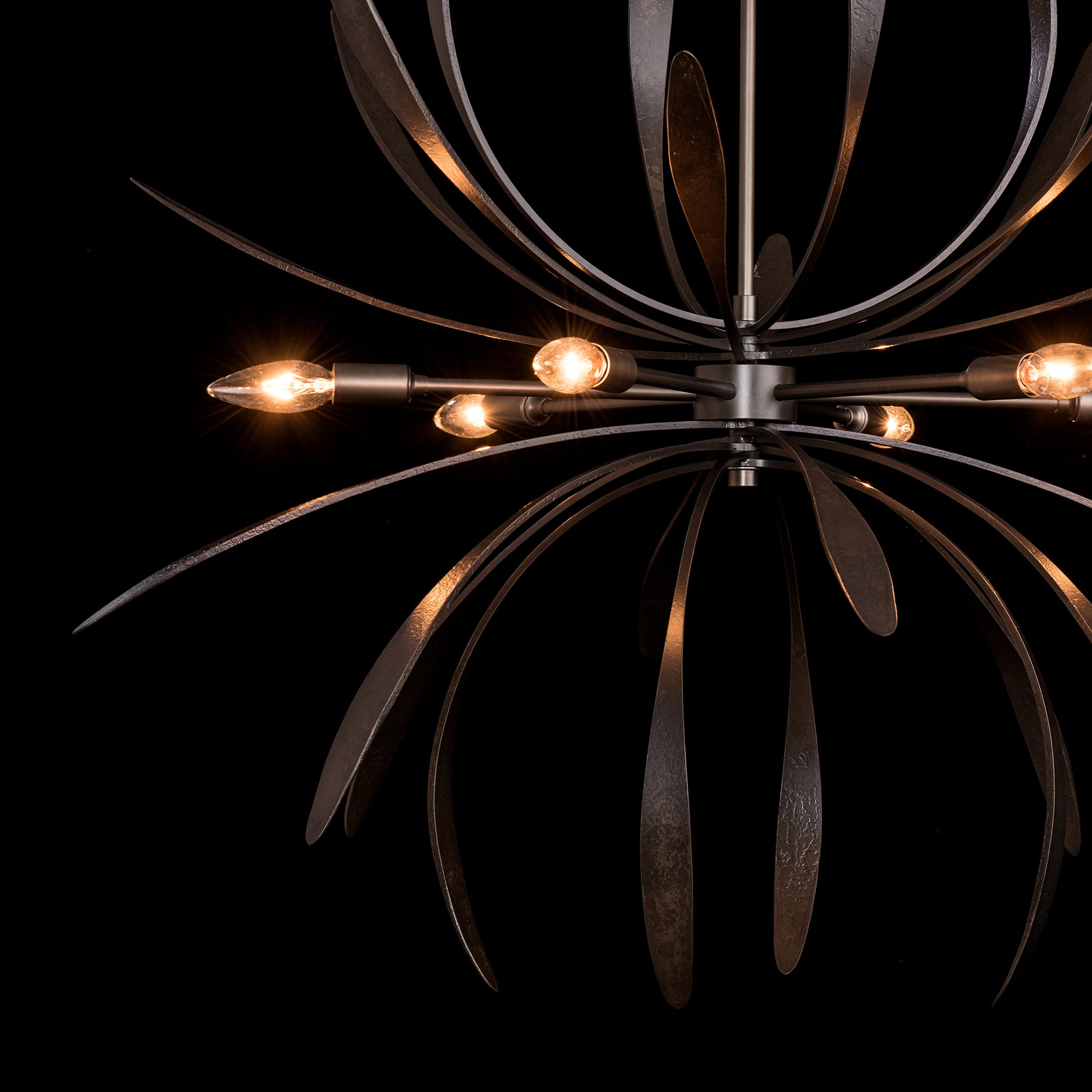 Dahlia Chandelier by Hubbardton Forge with leaf-like arms and glowing bulbs, crafted through eco-friendly metal forging.