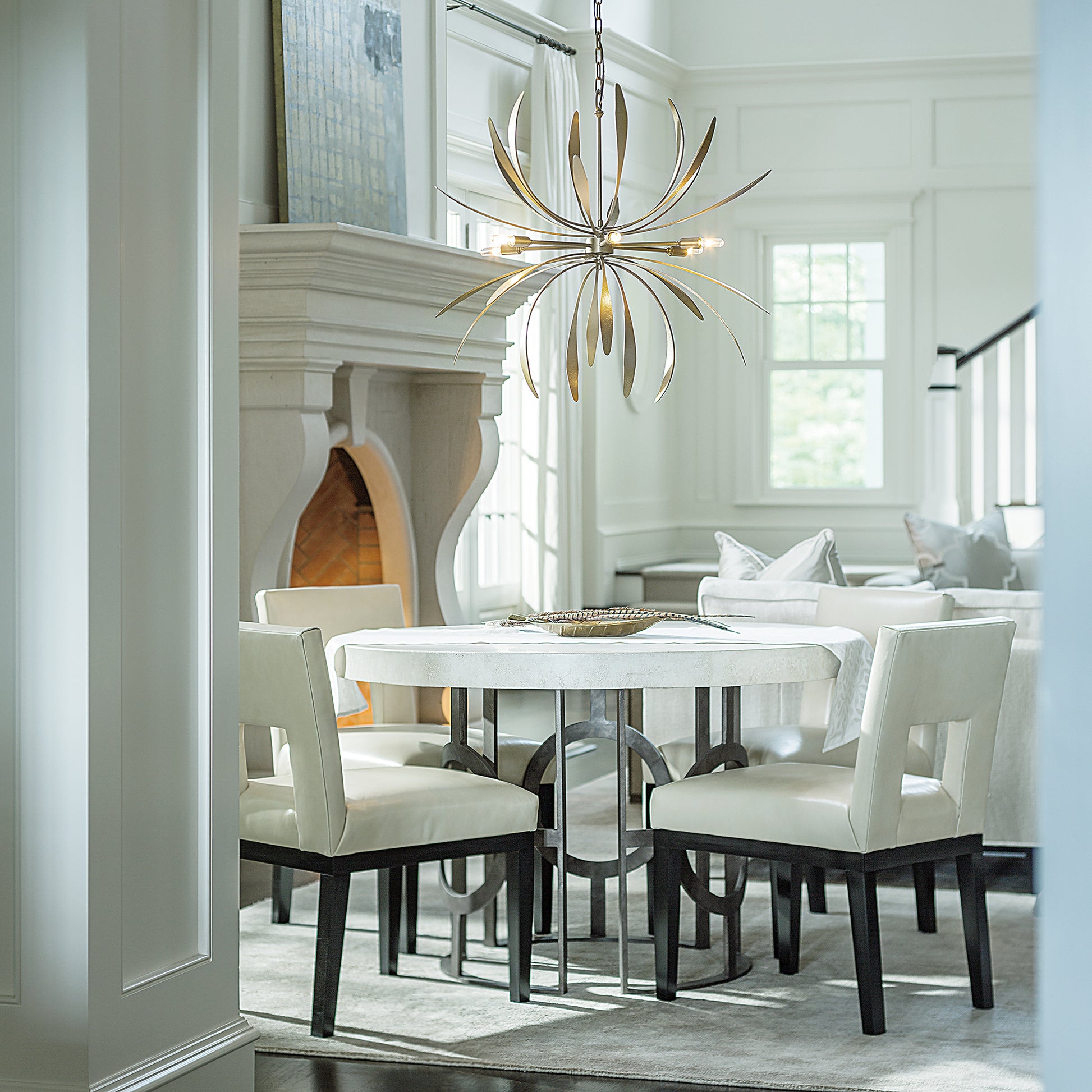 Round wooden dining table with four elegant white chairs, highlighted by a Hubbardton Forge Dahlia Chandelier.