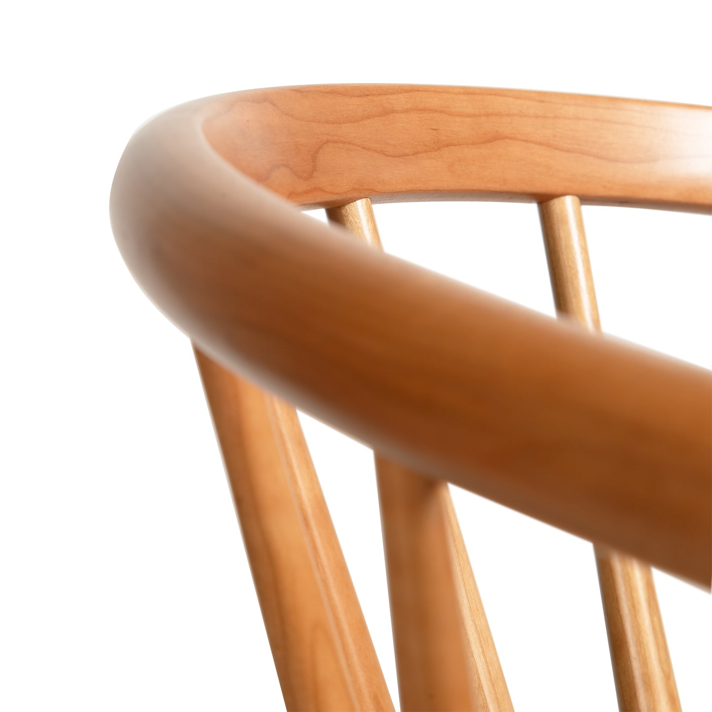 A close-up image of the top portion of a Dover Curveback Windsor Chair backrest, featuring smooth, rounded edges and vertical wooden slats. Crafted from sustainable solid wood by Vermont Woods Studios, the chair showcases a light, natural finish against a plain white background.