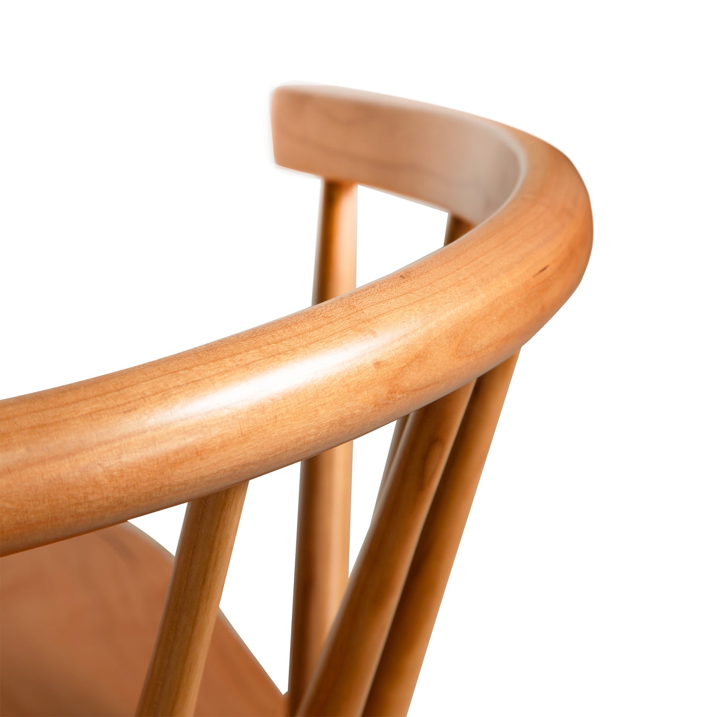 Close-up image of the Dover Curveback Windsor Chair - Display Model by Vermont Woods Studios, featuring a curved backrest. The light brown wood of the chair showcases a smooth, polished finish. Spindles connect the seat to the top of the backrest, creating a supportive design. The background is white.