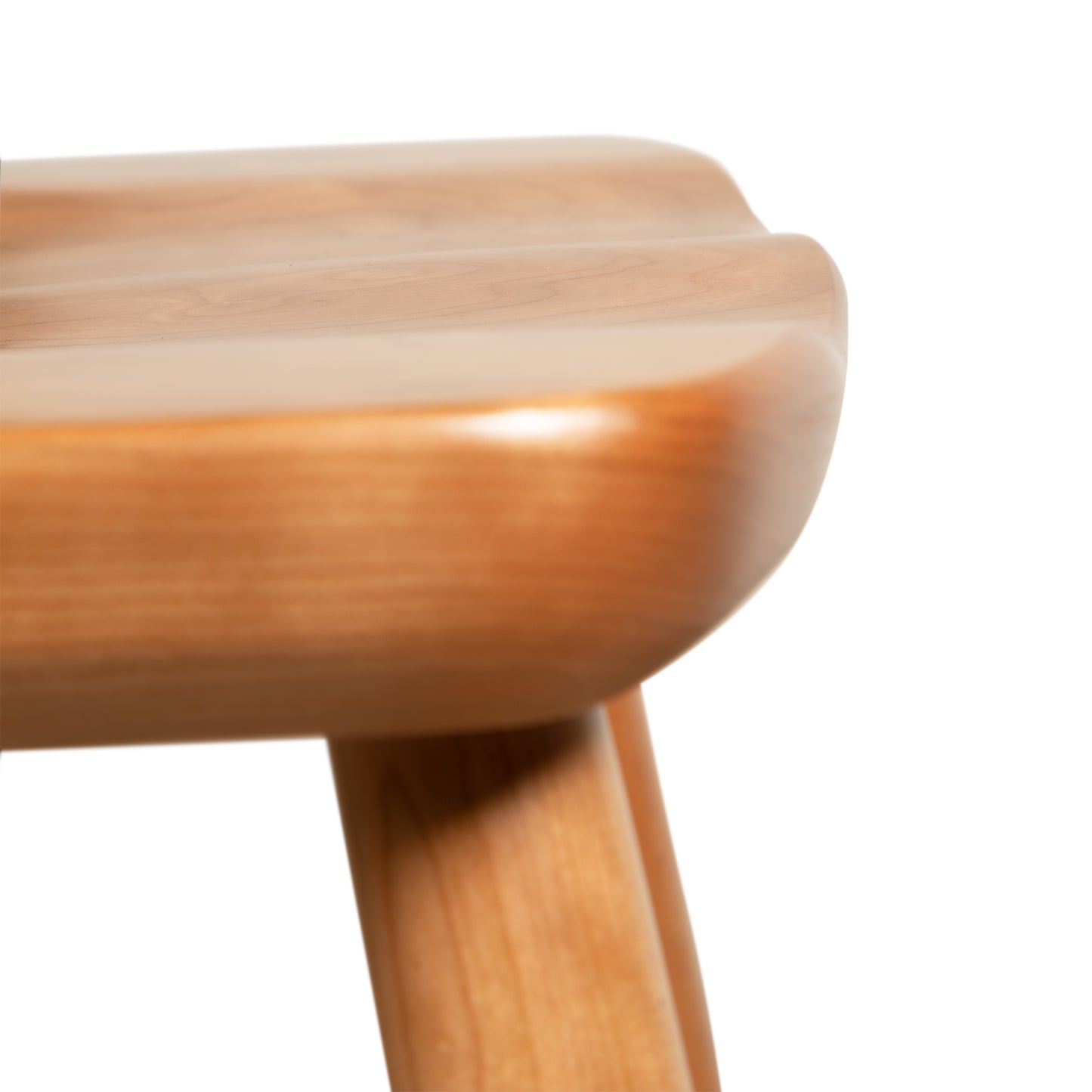 Close-up image of the Dover Curveback Windsor Chair - Display Model by Vermont Woods Studios, showing the corner where two legs meet a thick, polished seat. The wood has a smooth finish and sustainable solid wood construction, highlighting its refined craftsmanship. The background is completely white.