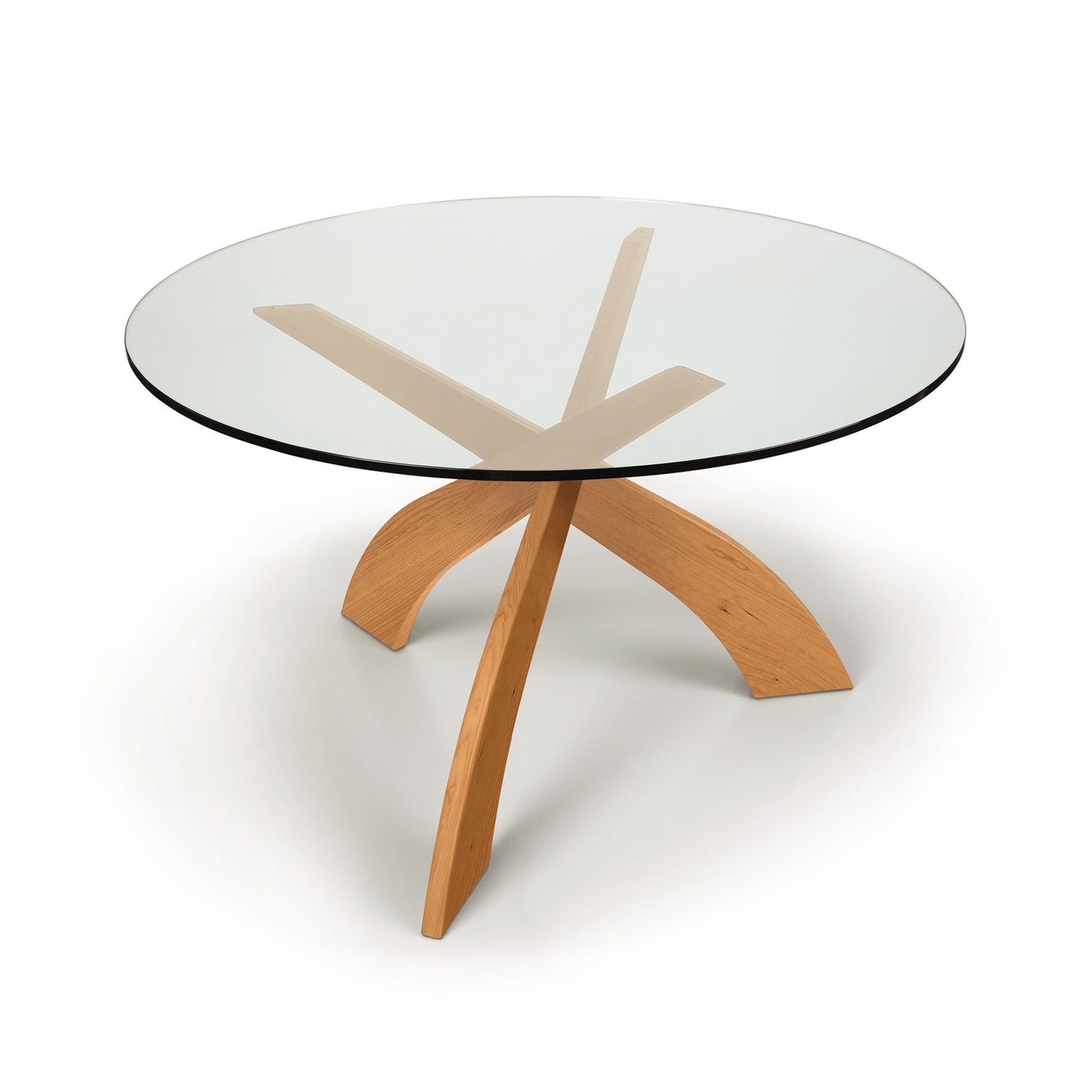 A modern Entwine Round Glass Top Dining Table with a tempered glass top and a cherry wood base featuring angular legs by Copeland Furniture.