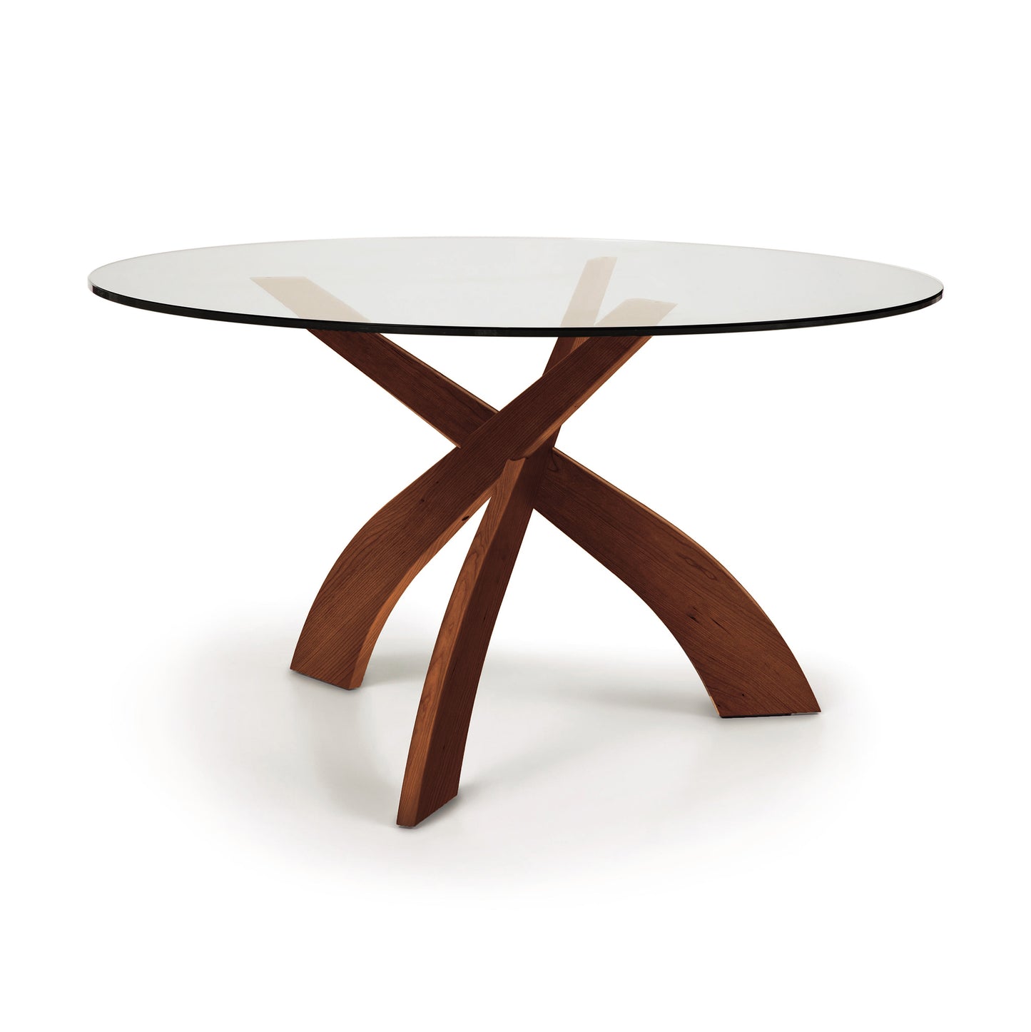 A Entwine Round Glass Top Dining Table with a tempered glass top and a wooden, cross-shaped base made of sustainably sourced cherry wood on a white background. Made by Copeland Furniture.