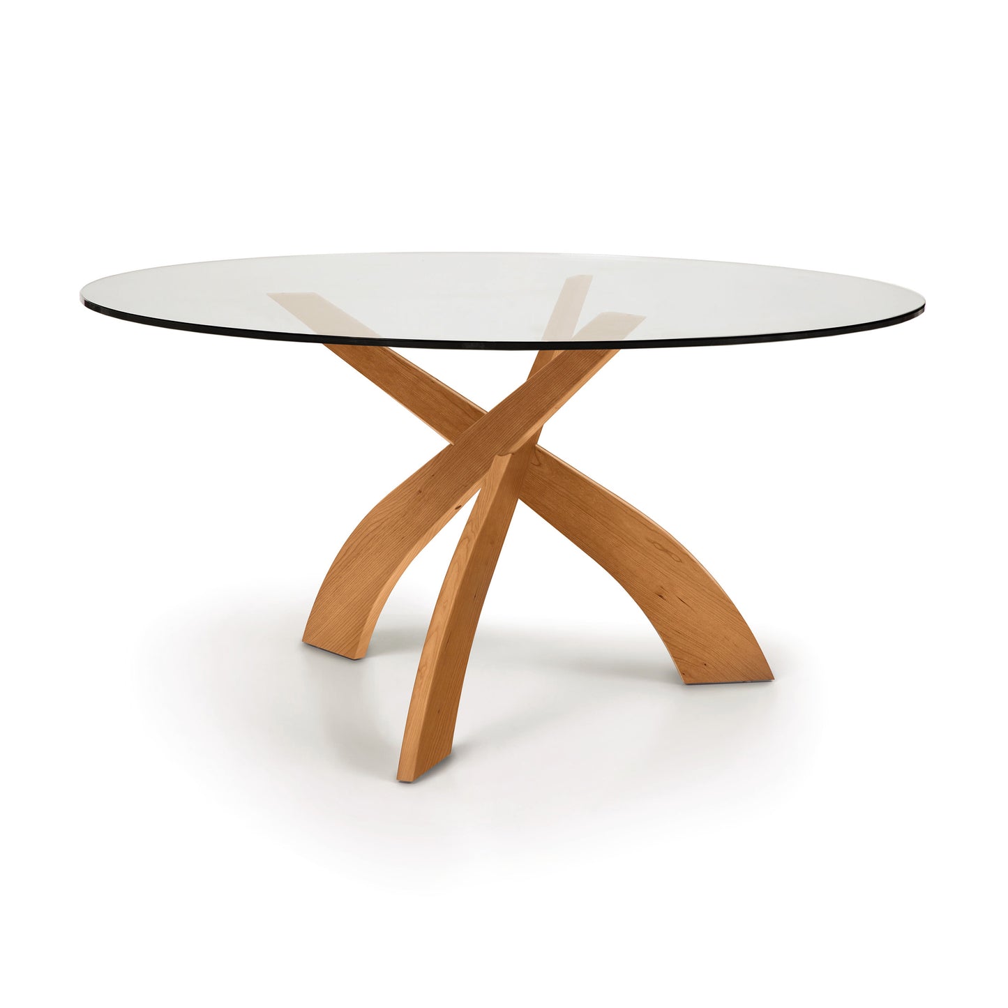 A Entwine Round Glass Top Dining Table with a sustainably sourced cherry wood cross base design on a white background by Copeland Furniture.