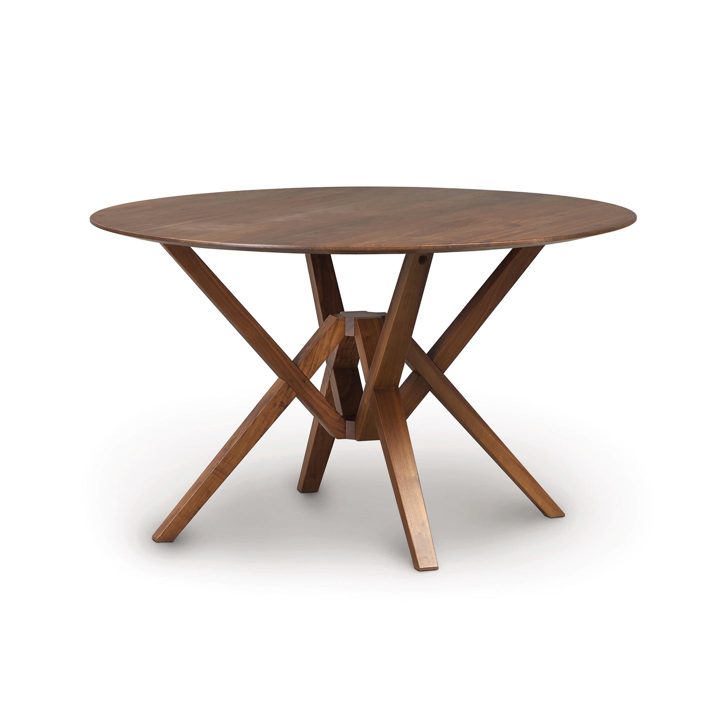 A round wooden table, known as the Copeland Furniture Exeter Round Solid Top Dining Table, crafted from sustainably harvested hardwoods with a crossed-leg support structure on a white background by Copeland.