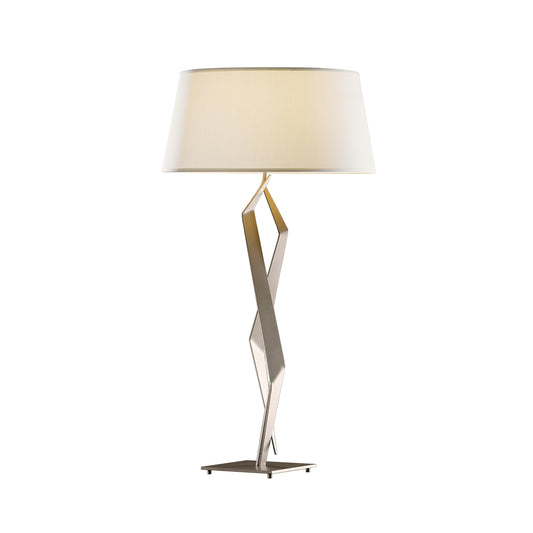 Facet Table Lamp by Hubbardton Forge with geometric metal stand and white fabric shade, highlighting its elegant handcrafted design.
