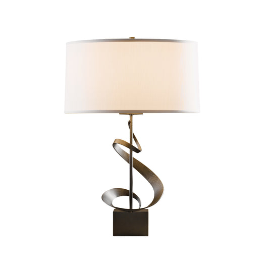 A modern Gallery Spiral Table Lamp by Hubbardton Forge with a hand-forged iron spiral base and a large, round, white lampshade, isolated on a white background.