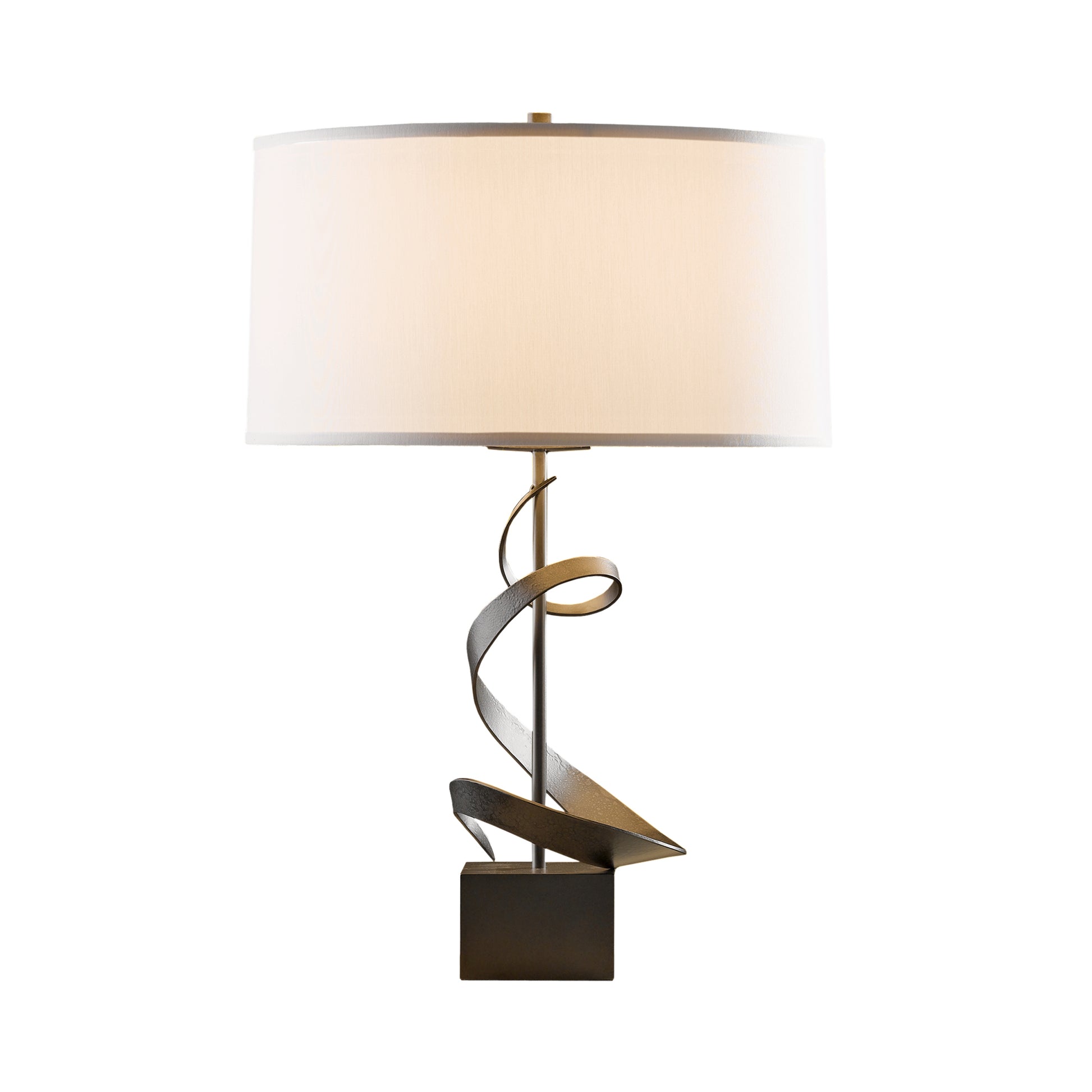 A modern Hubbardton Forge Spiral Table Lamp with a hand-forged iron base and a large, cylindrical cream shade, isolated on a white background.