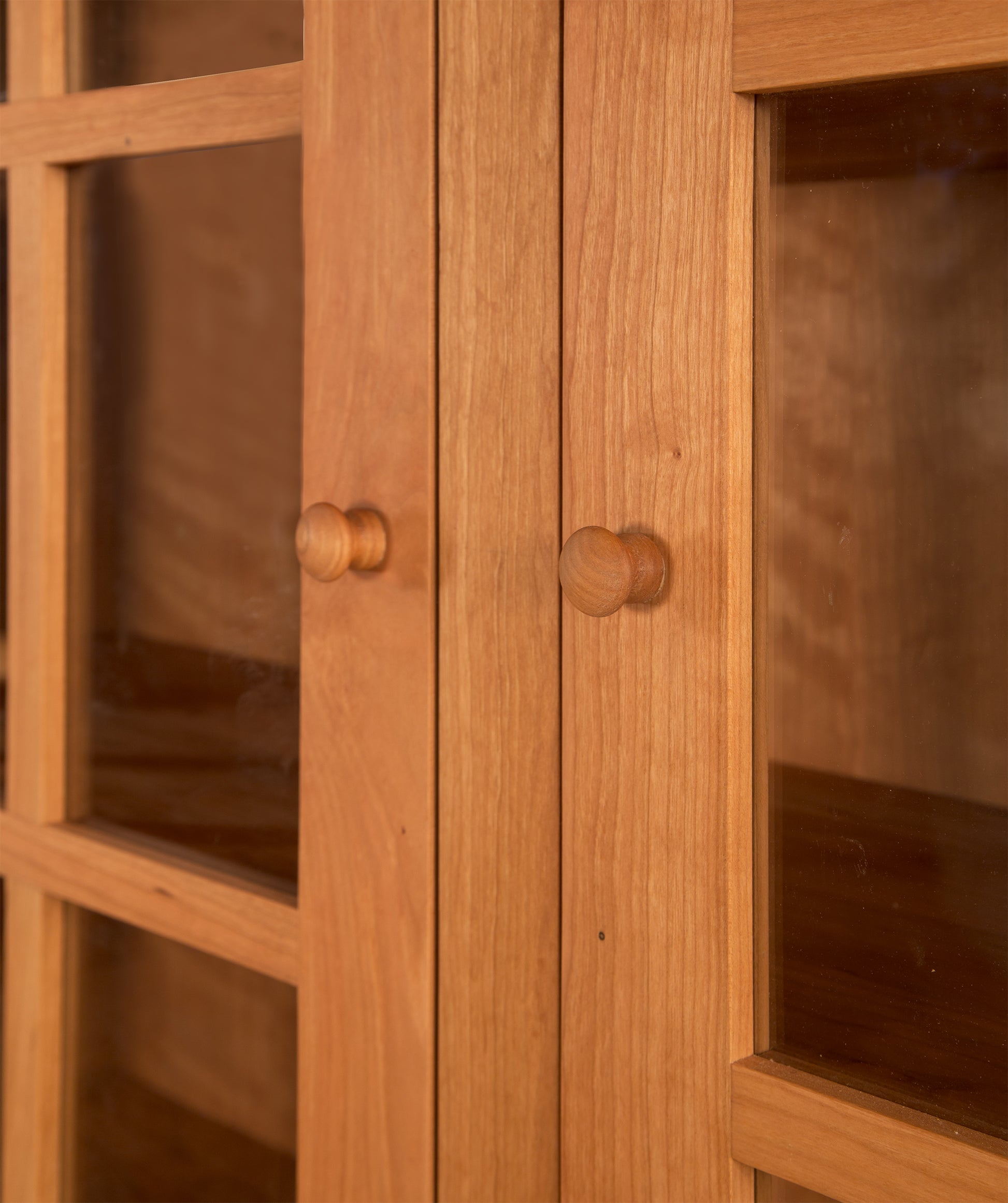 Wooden cabinet doors with round knobs, glass panels, and Heartwood Shaker Style from Vermont Furniture Designs.