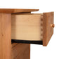 An open drawer revealing dovetail joint construction and a wooden knob from the sustainably harvested North American hardwoods, isolated on a white background, featuring the Heartwood Shaker Vertical File Cabinet by Vermont Furniture Designs.