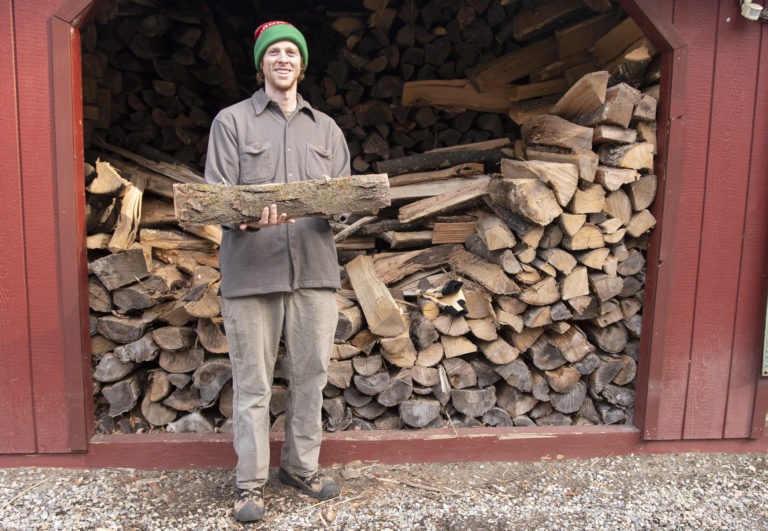 A man standing in front of a pile of wood.