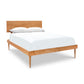 A Larssen Bed by Vermont Furniture Designs, featuring a Mid-century modern design wooden bed frame with a headboard, fitted with white bedding and two pillows, isolated on a white background.